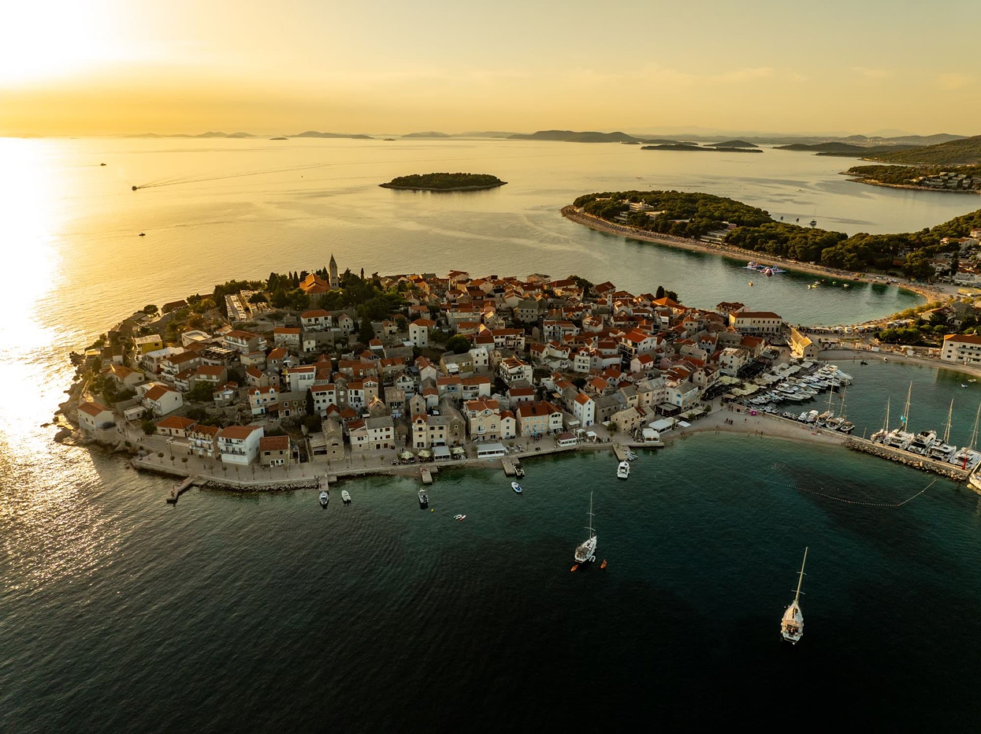 Scenic aerial view of Primošten, Croatia, showcasing its picturesque coastline and sunset hues.