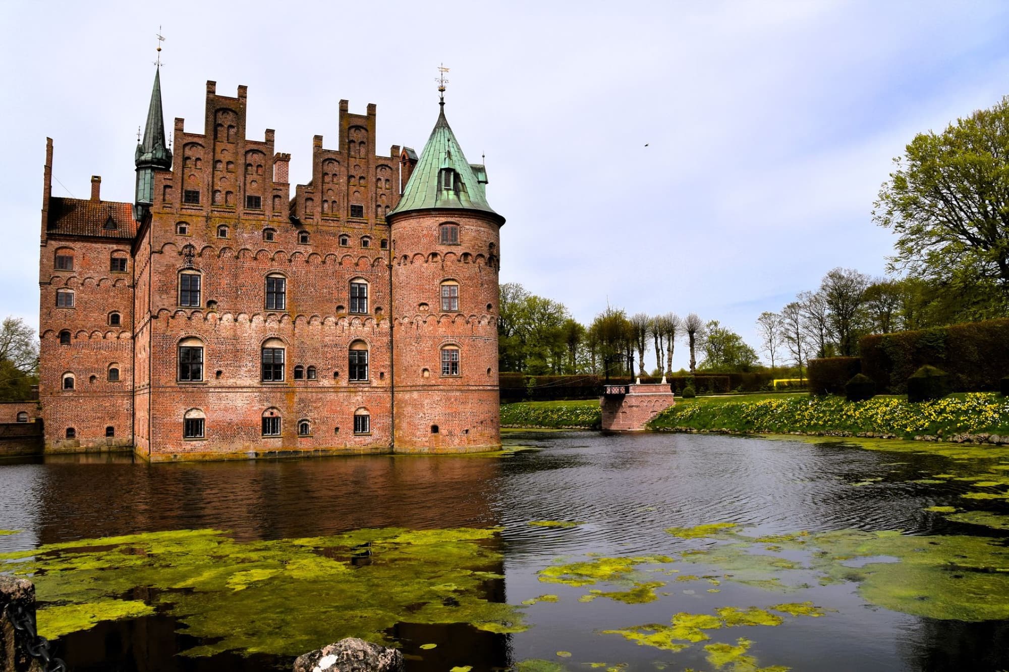 Egeskov Castle in Denmark beautifully reflected in its surrounding moat on a clear spring day.