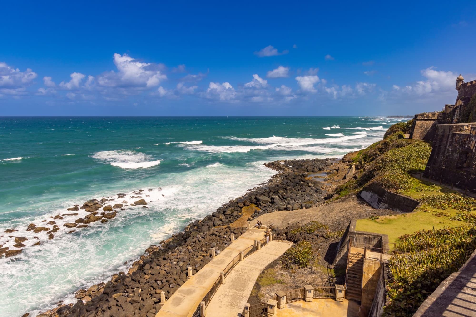 Breathtaking aerial view of San Juan's rocky coast and clear blue sea under a sunny sky.