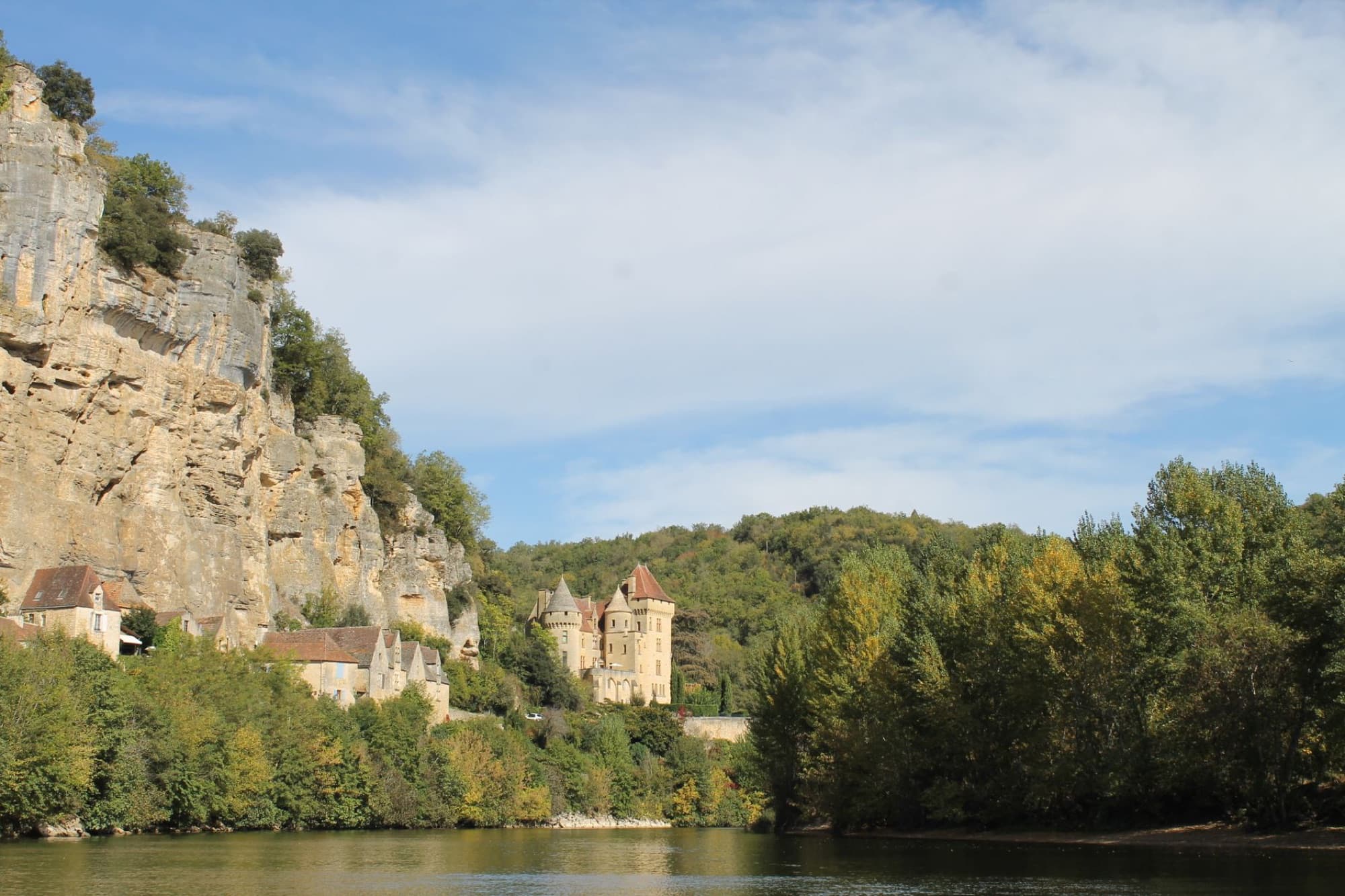 Scenic view of a historic French château perched on cliffs by a tranquil river, surrounded by lush greenery.