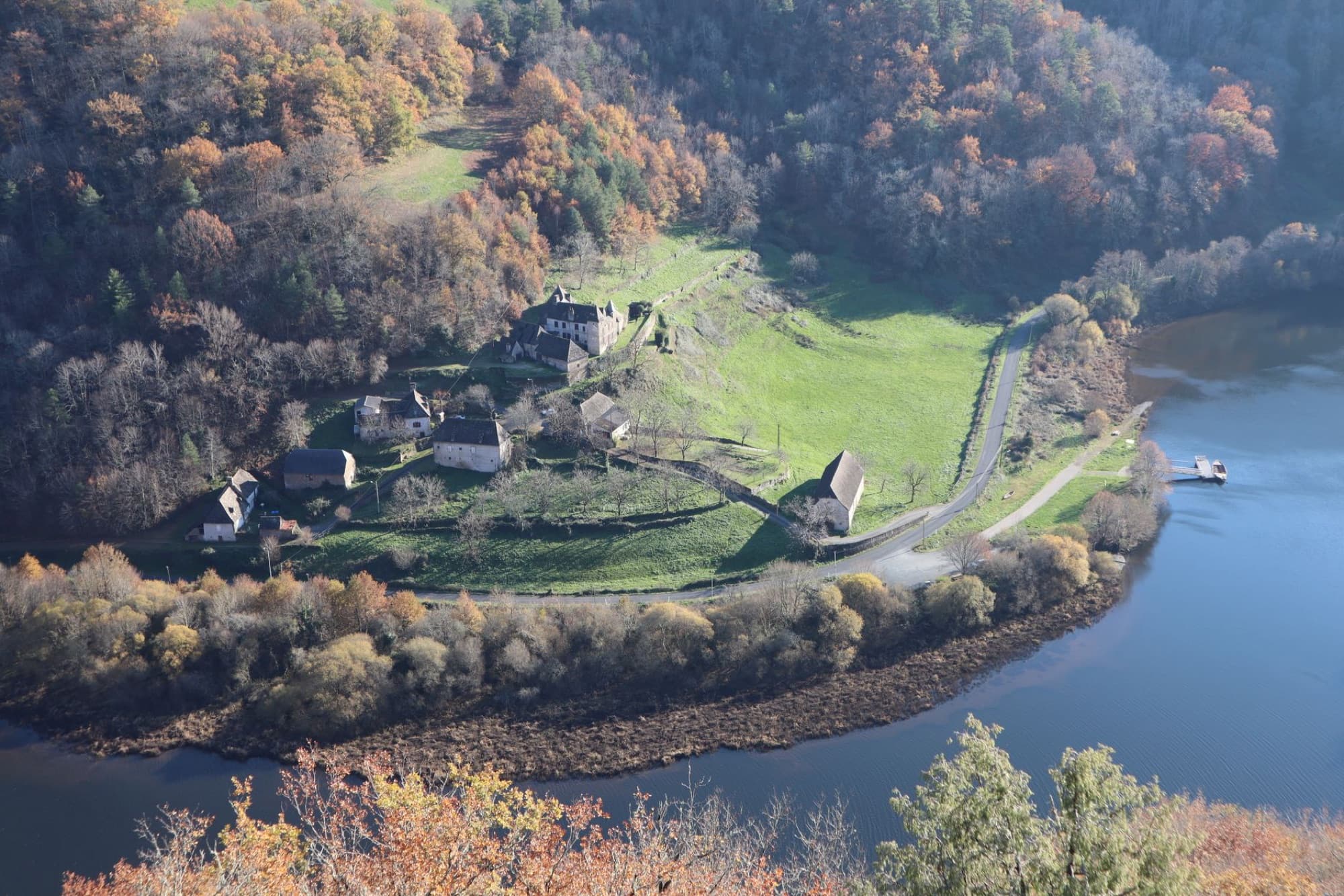 Scenic aerial shot of secluded farmhouse amidst autumn foliage and a river in Corrèze, France.