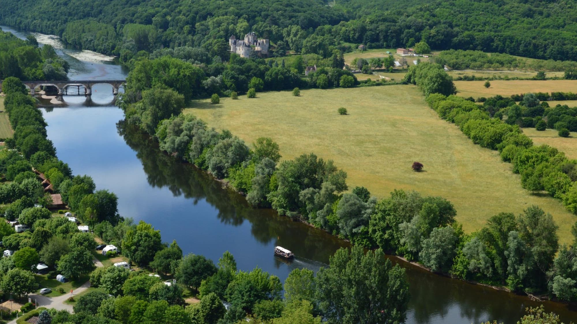 A scenic aerial view of a lush riverside landscape featuring a historic bridge and dense greenery.