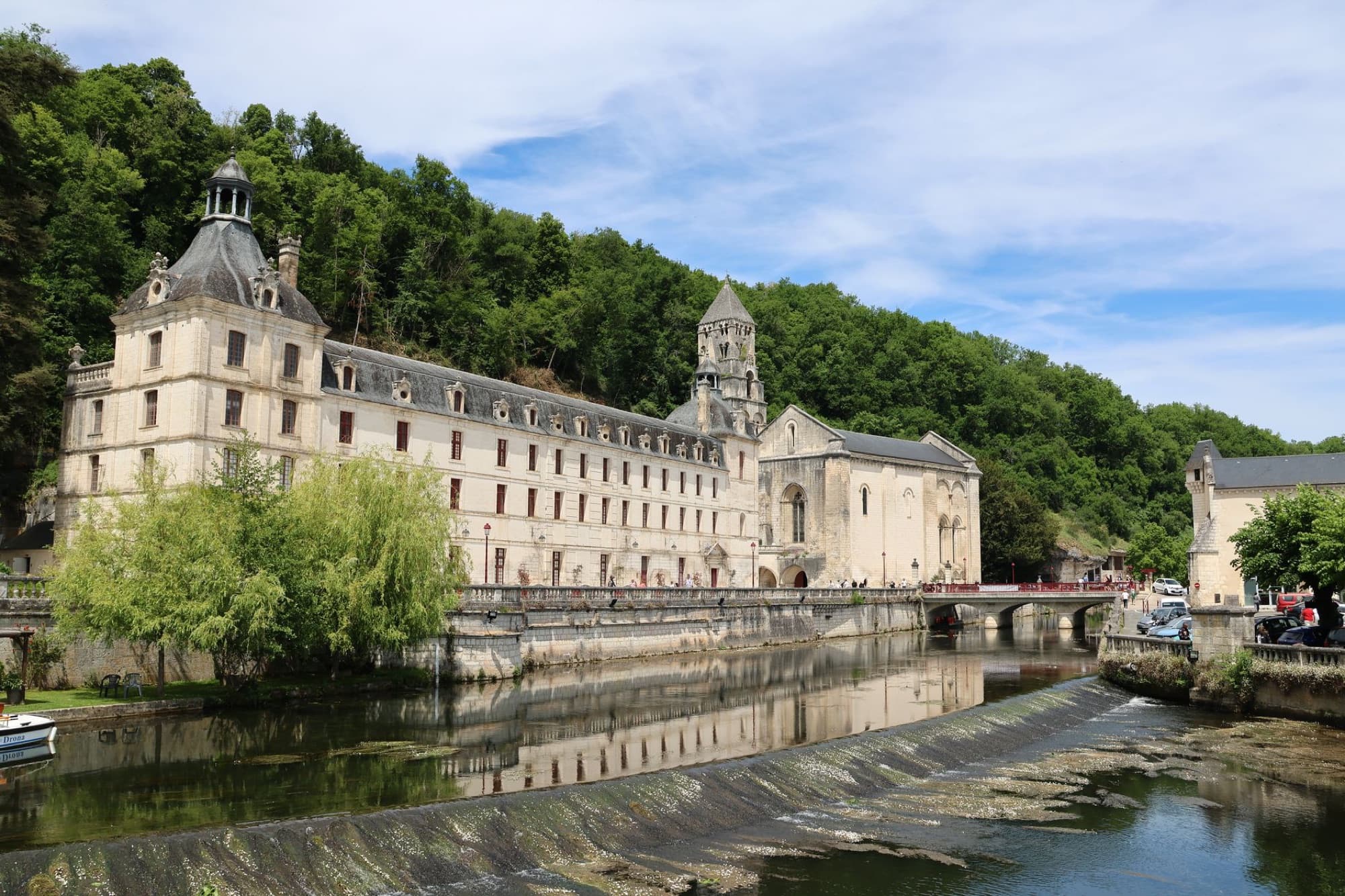 Brantôme Abbey in France with scenic river view and lush greenery.