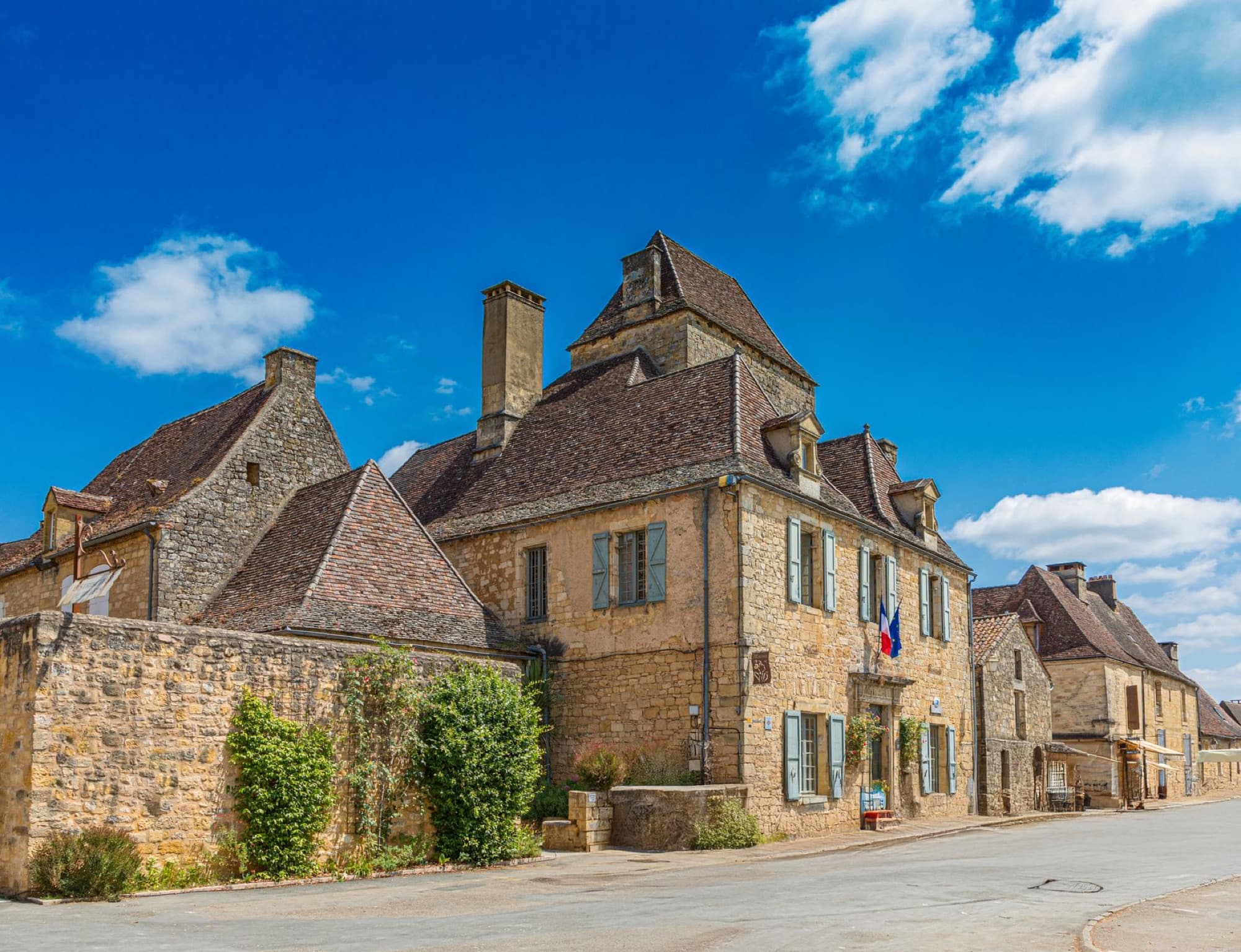 Charming street scene of a historic French village with stone buildings under a blue sky.