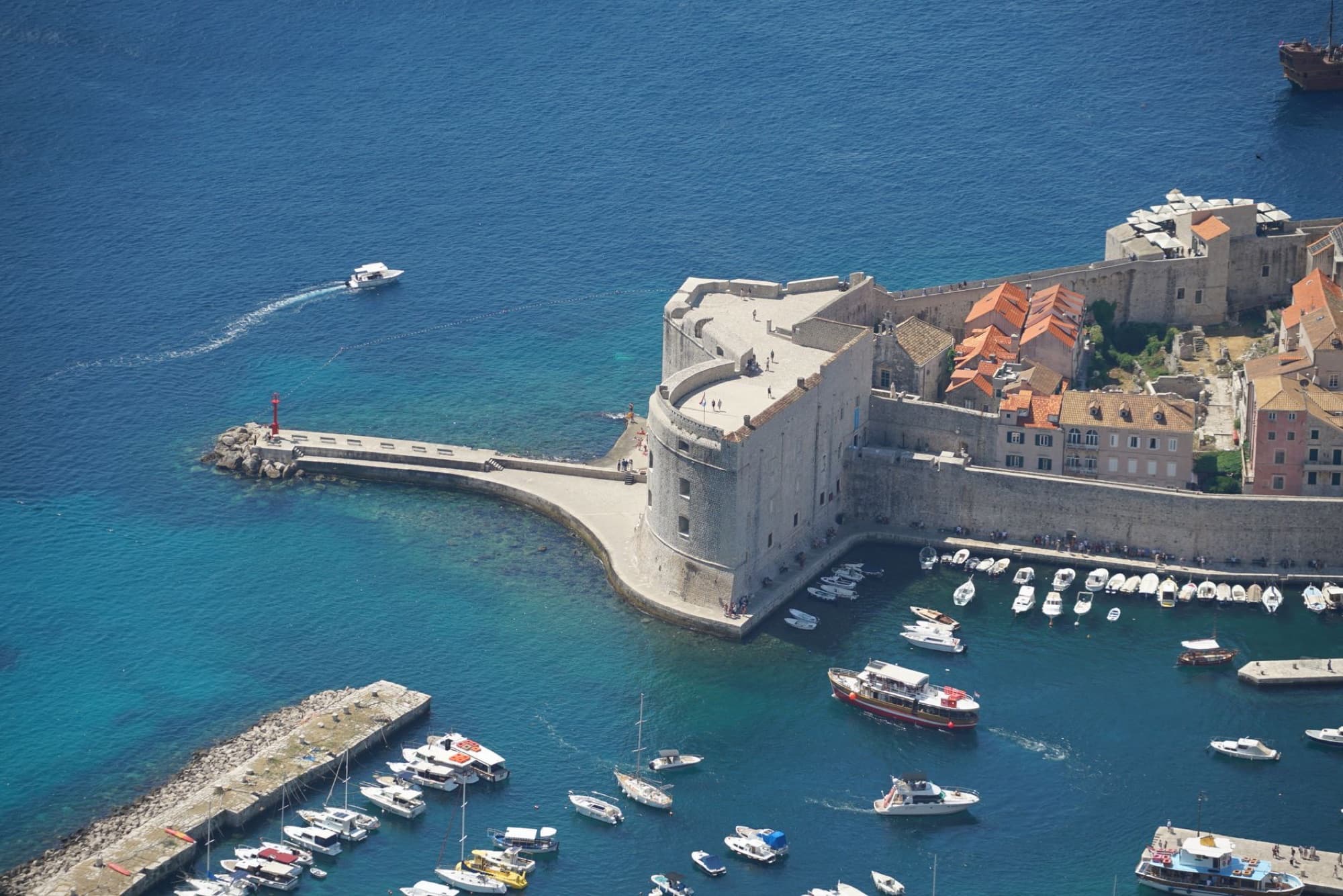 A stunning aerial panorama of Dubrovnik's historic harbor and St. John's Fort on a sunny day.