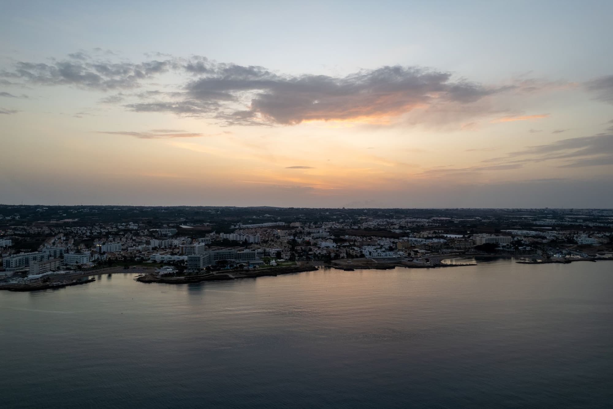 Serene aerial view of Pernera coastline at sunset, showcasing the tranquil sea and cityscape of Famagusta, Cyprus.