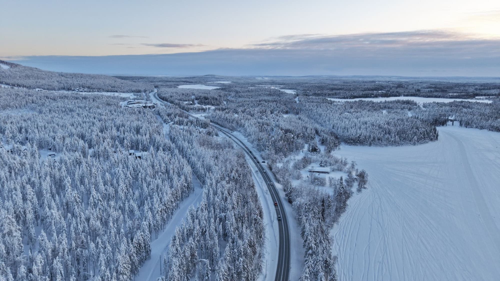 Aerial shot of a snowy road winding through a winter forest in Finland, at sunset.