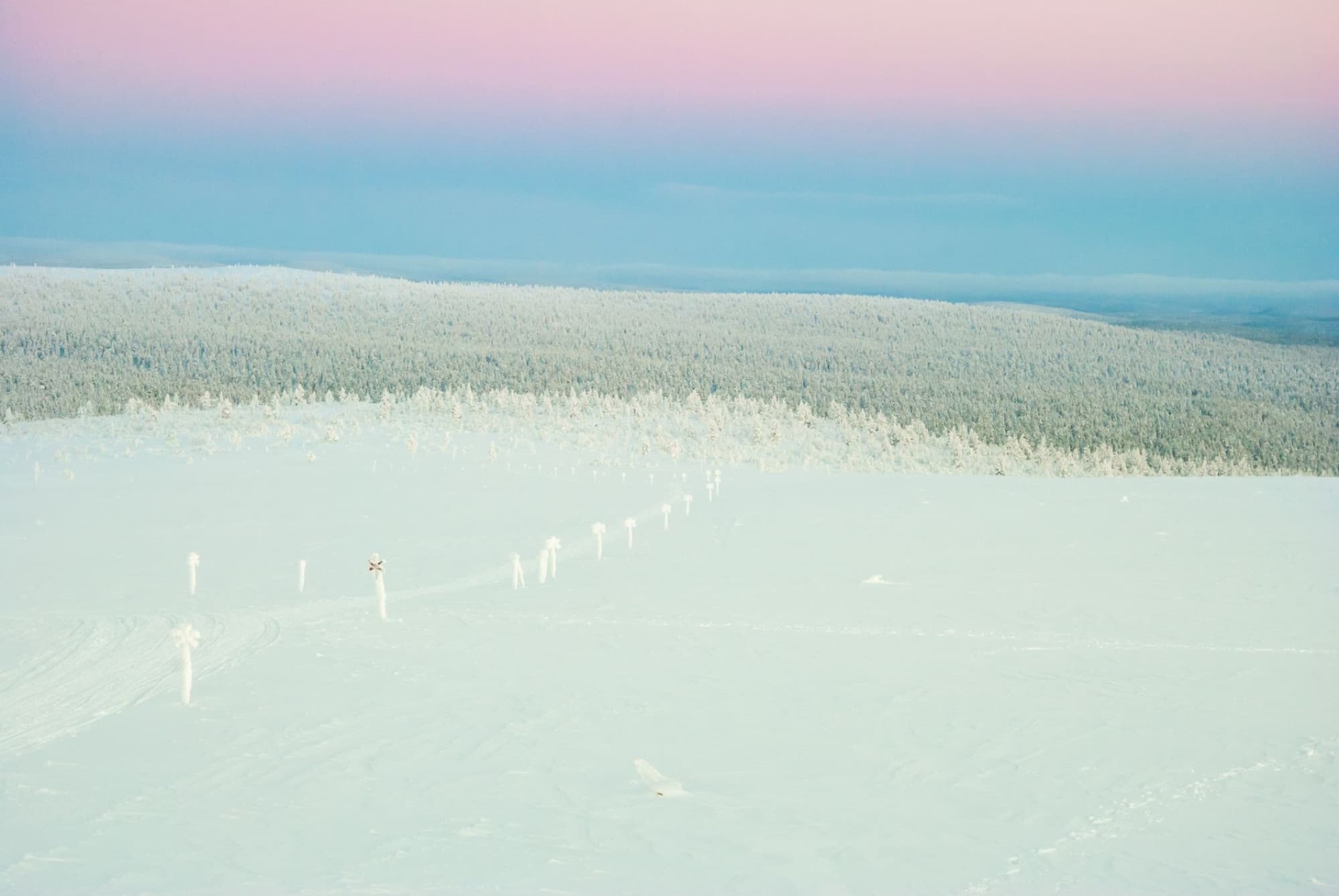 An aerial view of the snow-covered landscape in Saariselkä, Finland, during twilight with colorful skies.