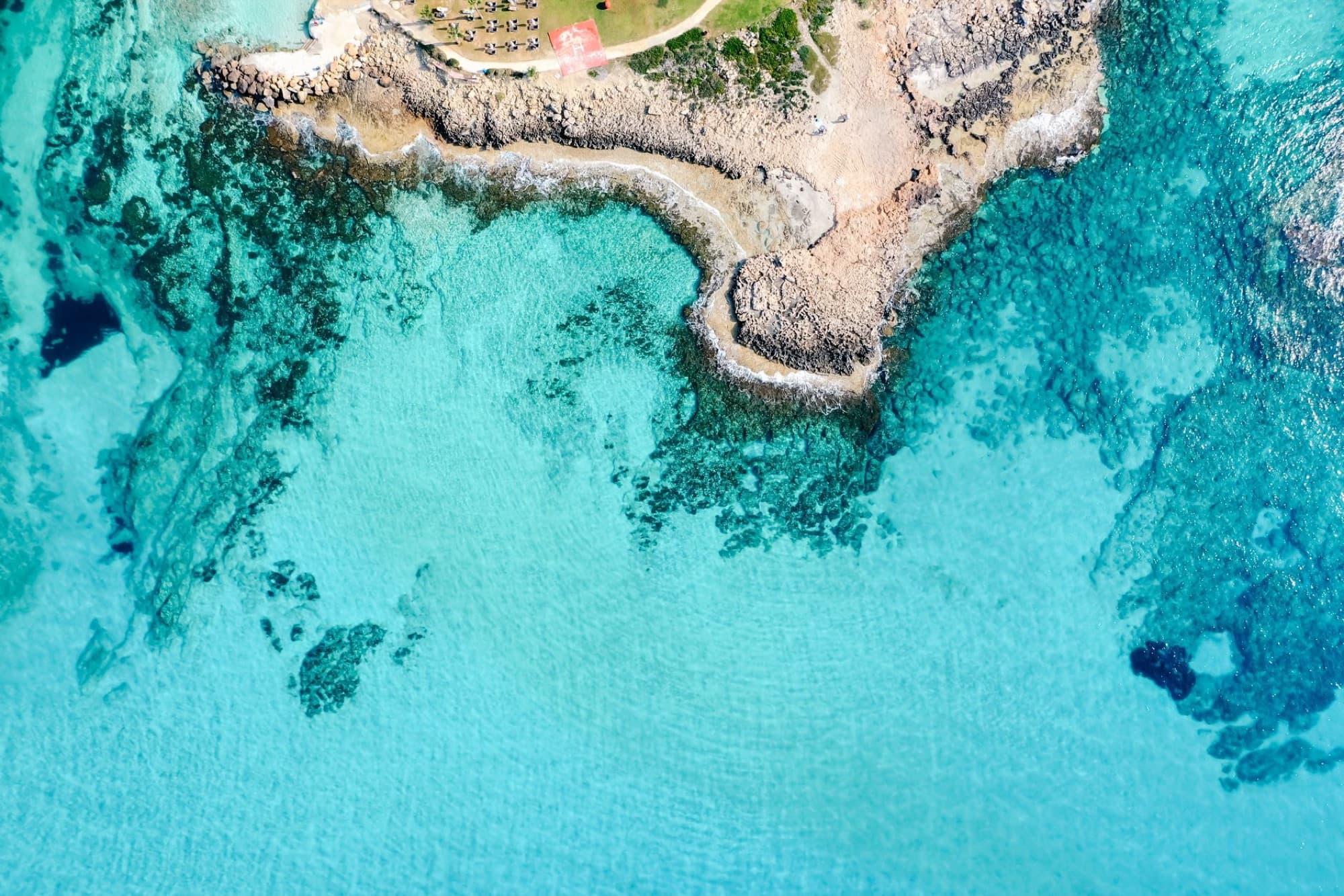 Aerial view of a beautiful turquoise seashore with clear water and rocky coastline.