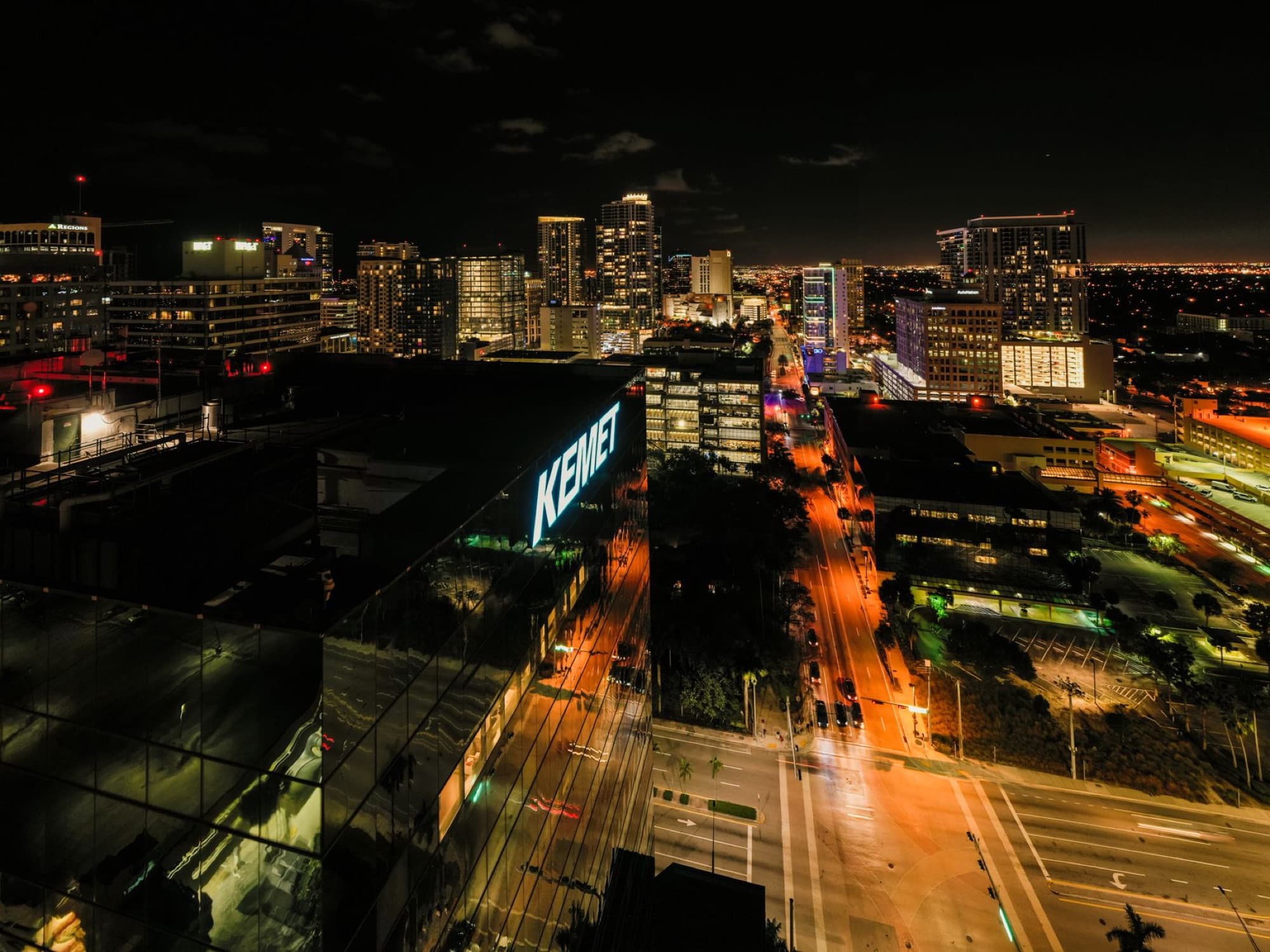 Drone view of asphalt roads between illuminated multistory buildings at night in Fort Lauderdale city