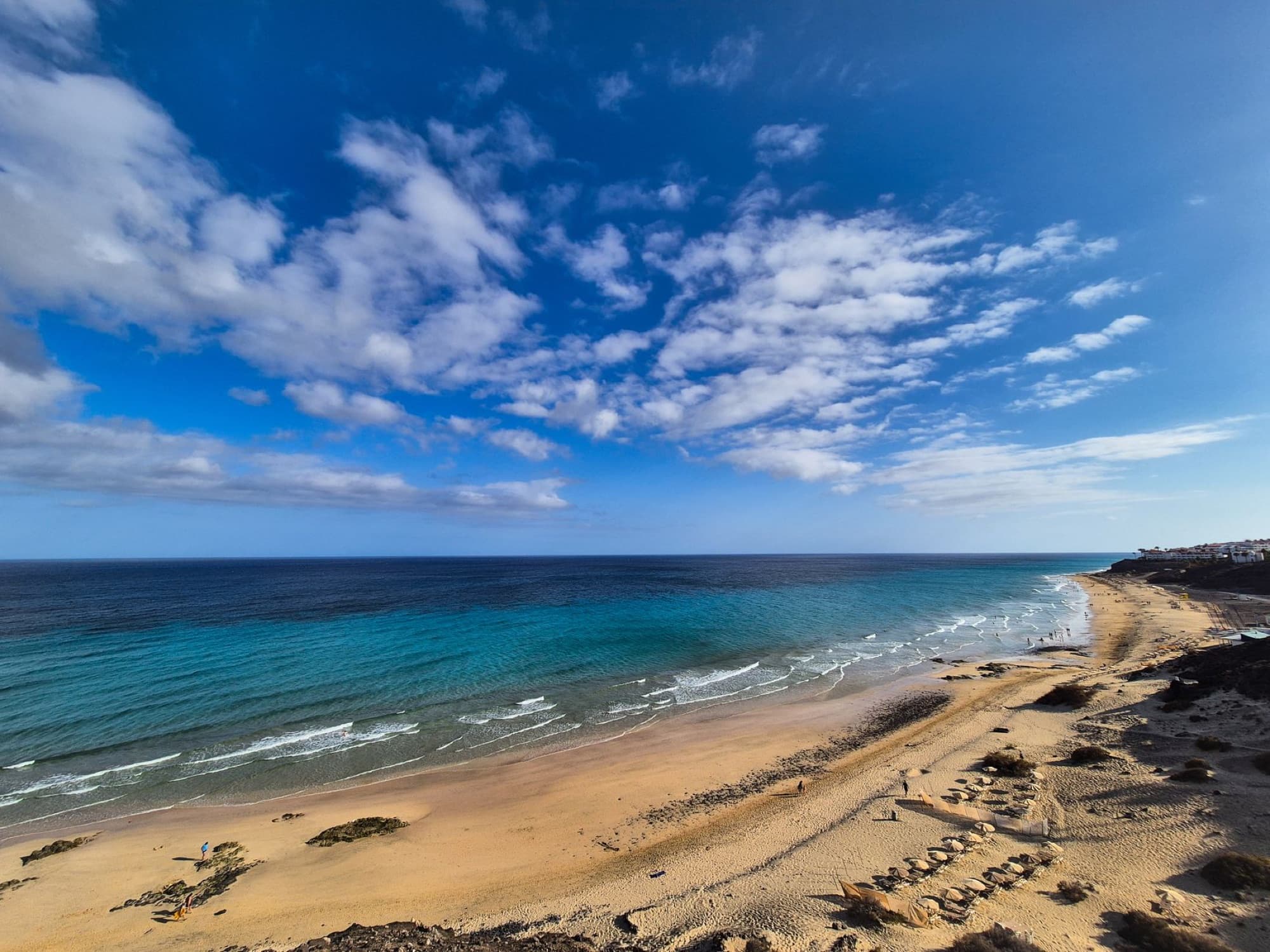 Explore a pristine beach in Fuerteventura with crystal-clear waters beneath a bright blue sky.