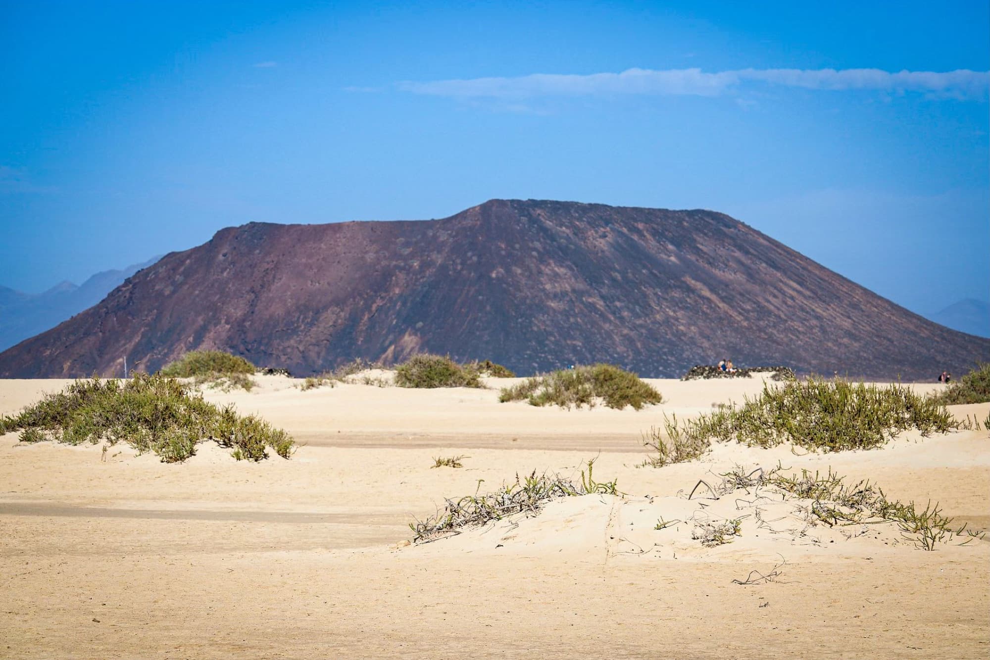 Arid volcanic landscape with sand dunes and sparse vegetation in Fuerteventura, Spain.