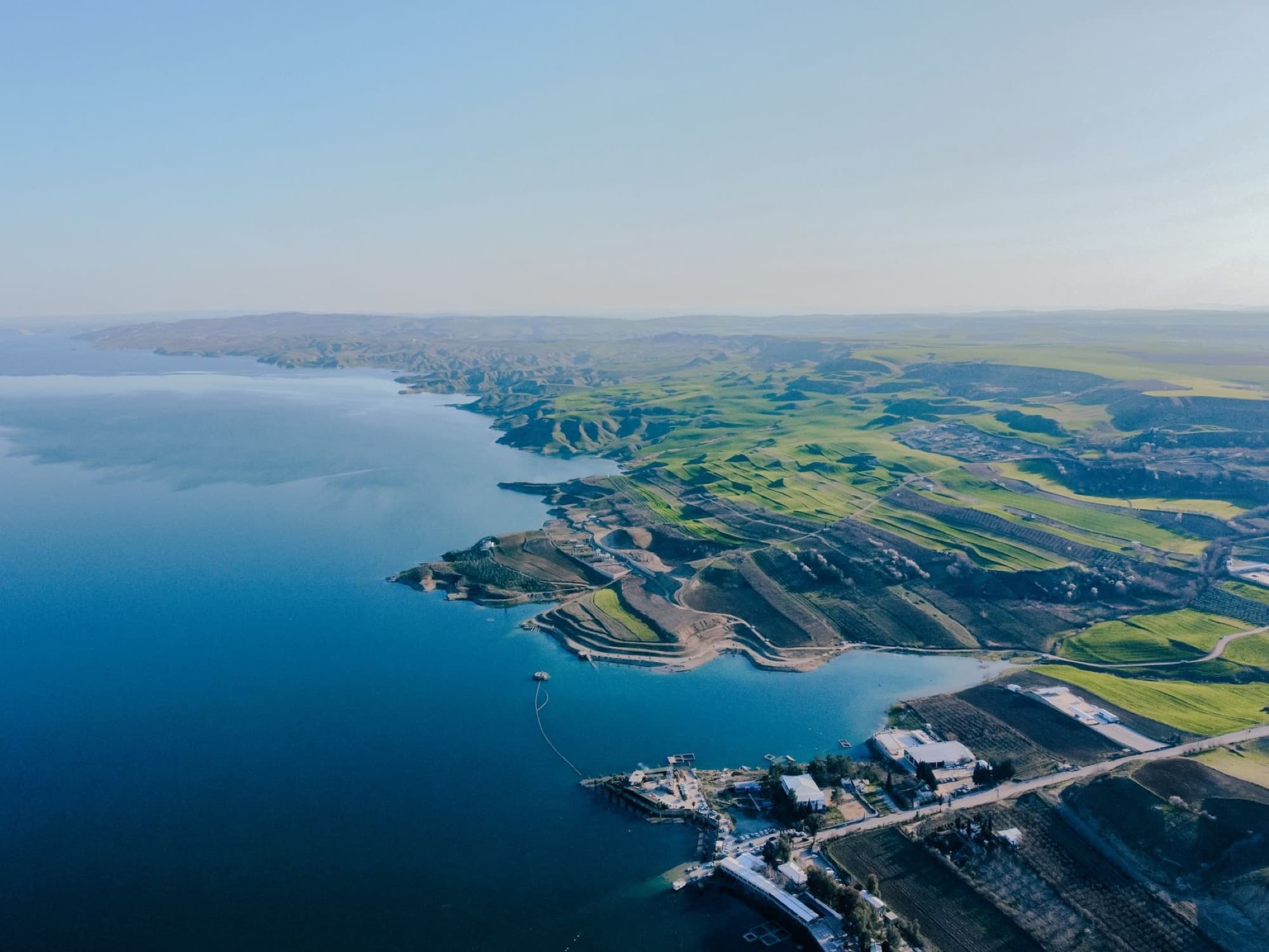 Stunning aerial shot of scenic coastline with rolling green hills and a clear blue sky.