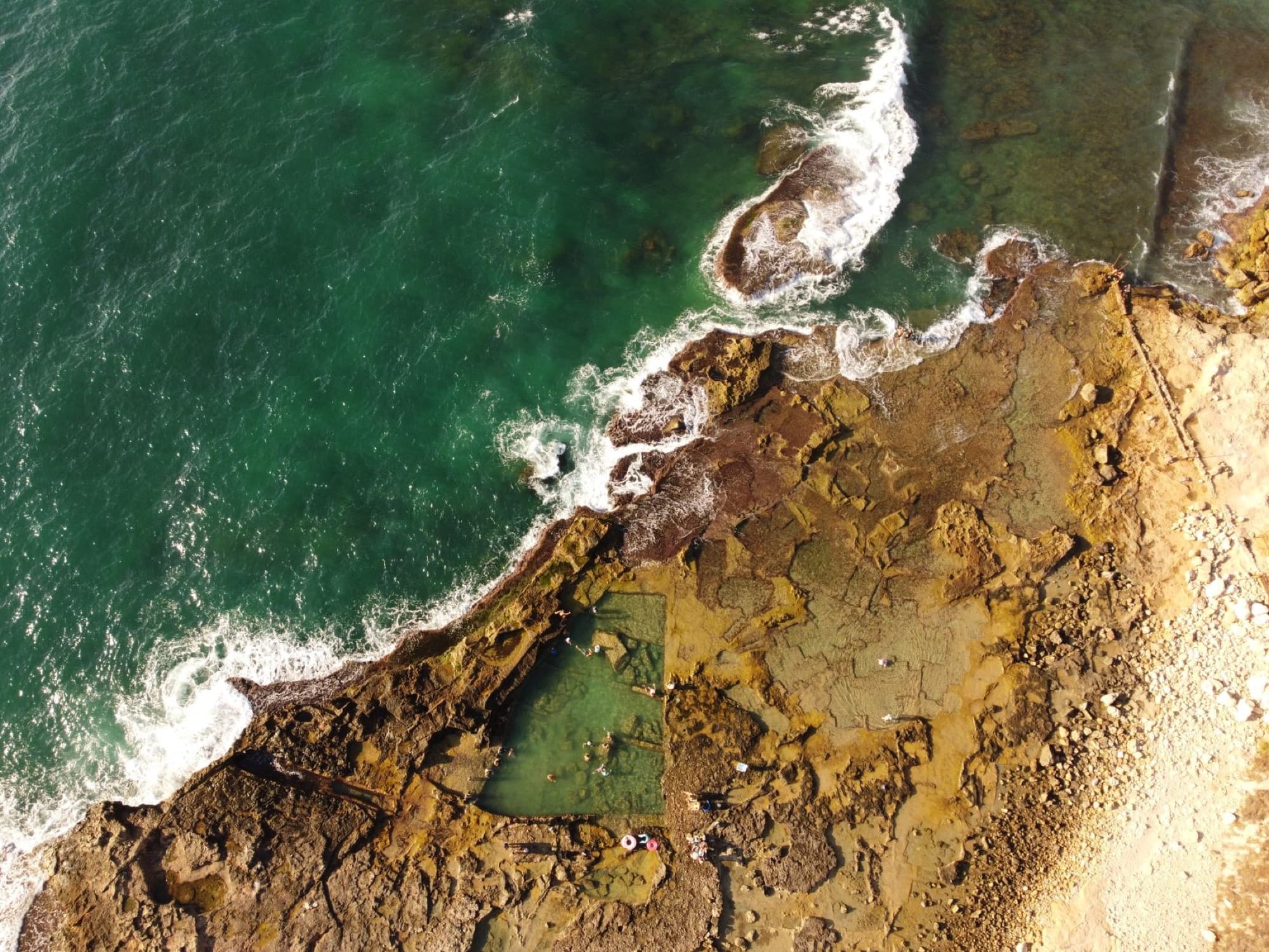 Drone shot capturing the rugged coastline of Akko, Israel with turquoise sea waves crashing against the rocky shore.