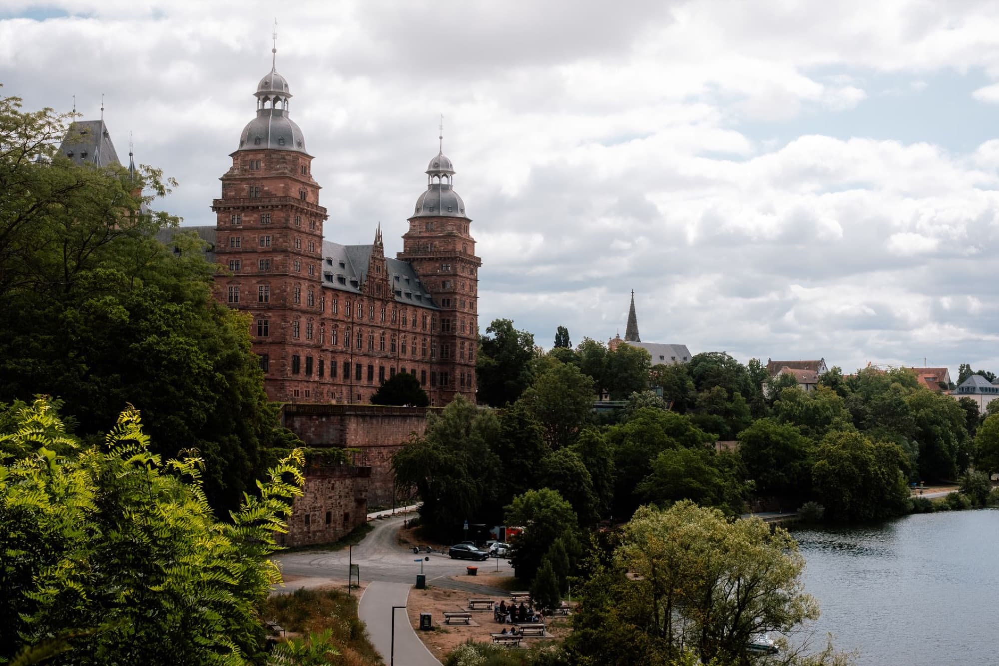 Scenic view of Schloss Johannisburg and river in Aschaffenburg, Germany surrounded by lush greenery.