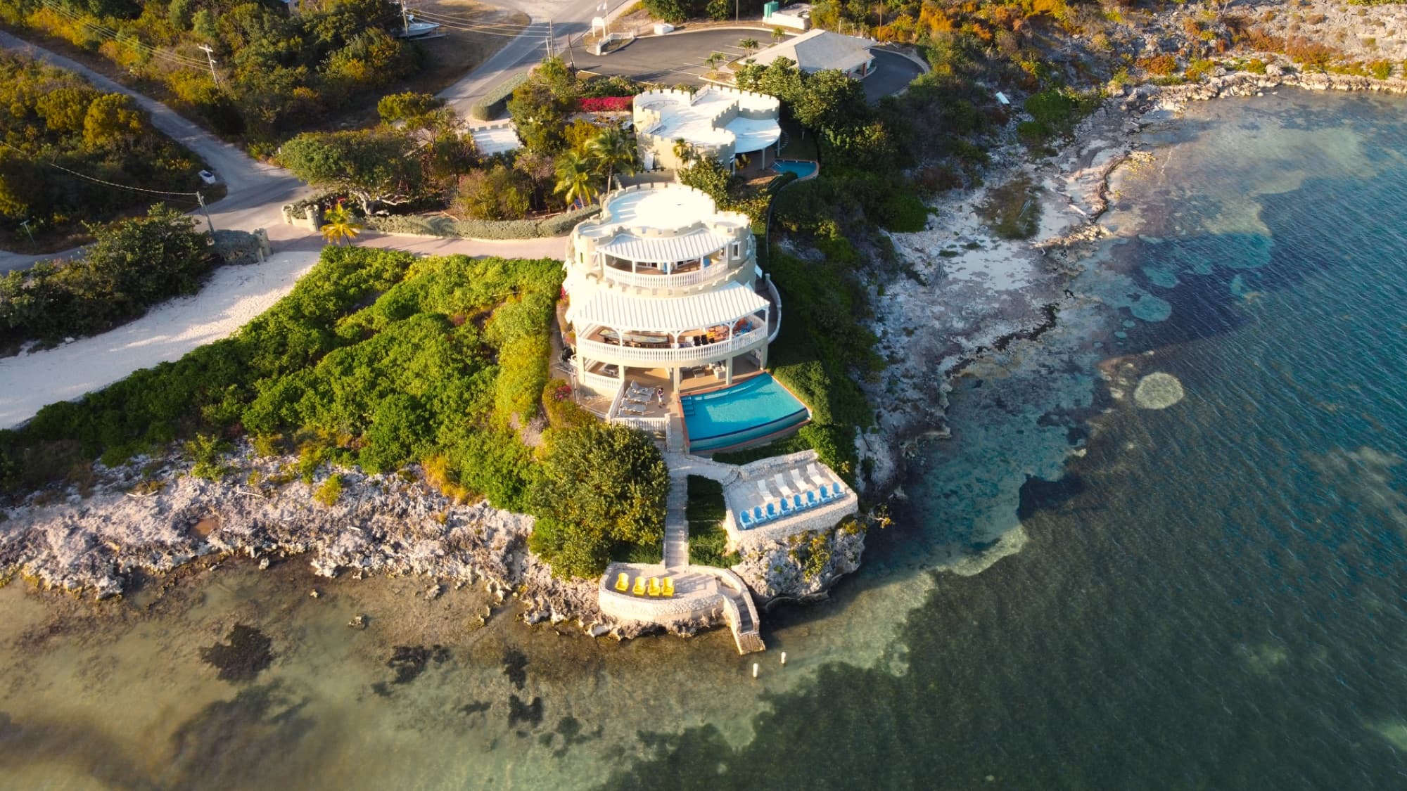 A stunning aerial view of a luxury villa on Grand Cayman with a seafront pool and lush greenery.