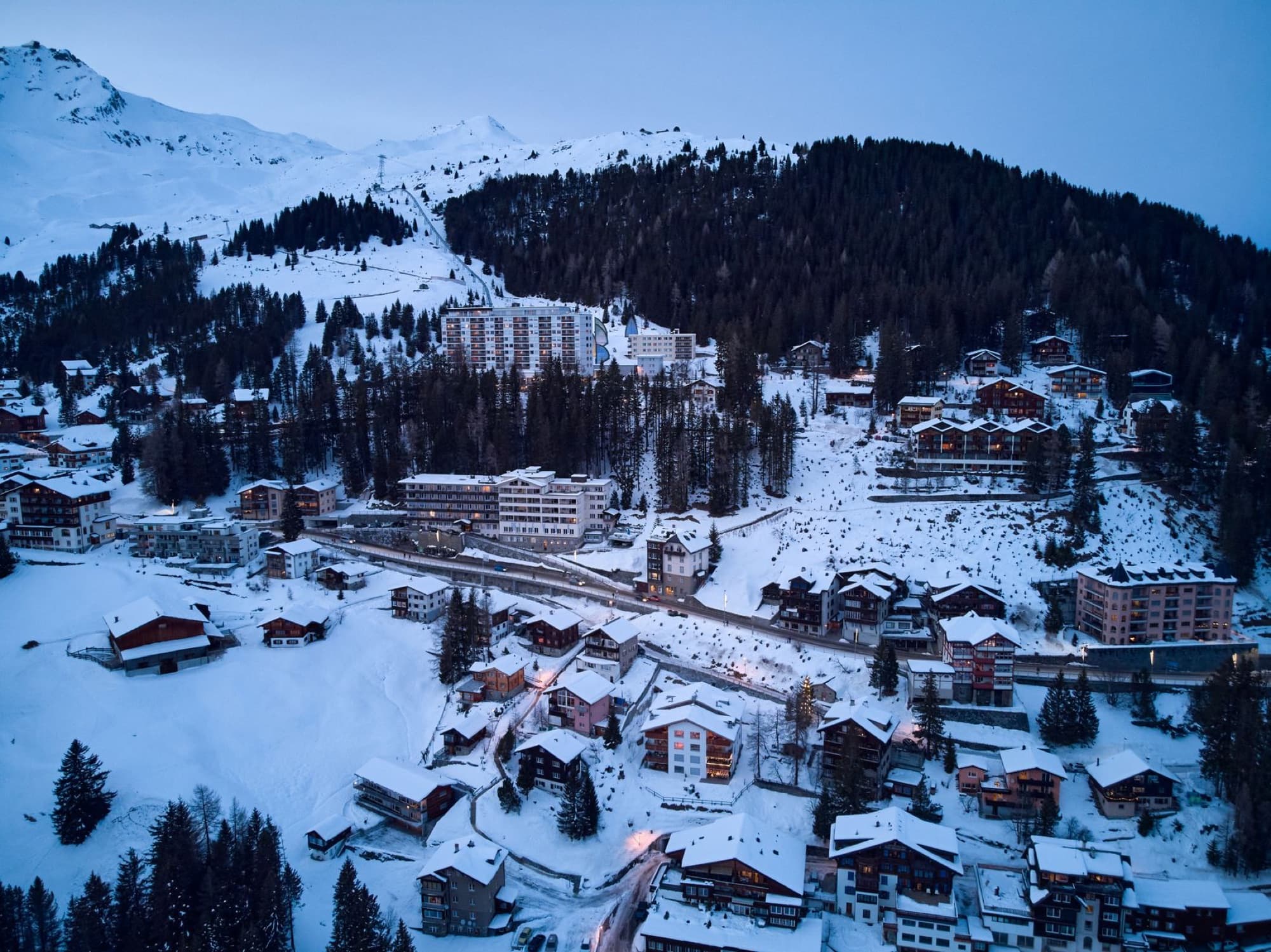 A breathtaking aerial view of the snowy Arosa village in Switzerland during winter, showcasing picturesque buildings and mountains.