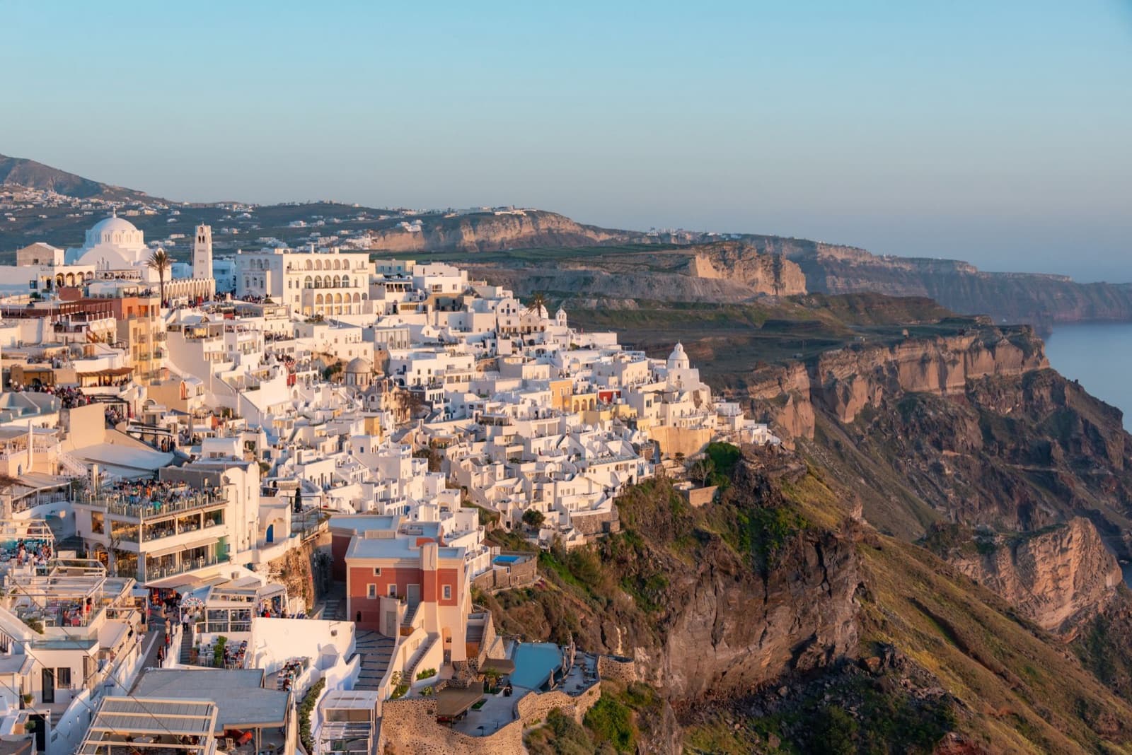 Spectacular aerial view of whitewashed buildings atop the cliffs of Santorini, Greece at sunset.