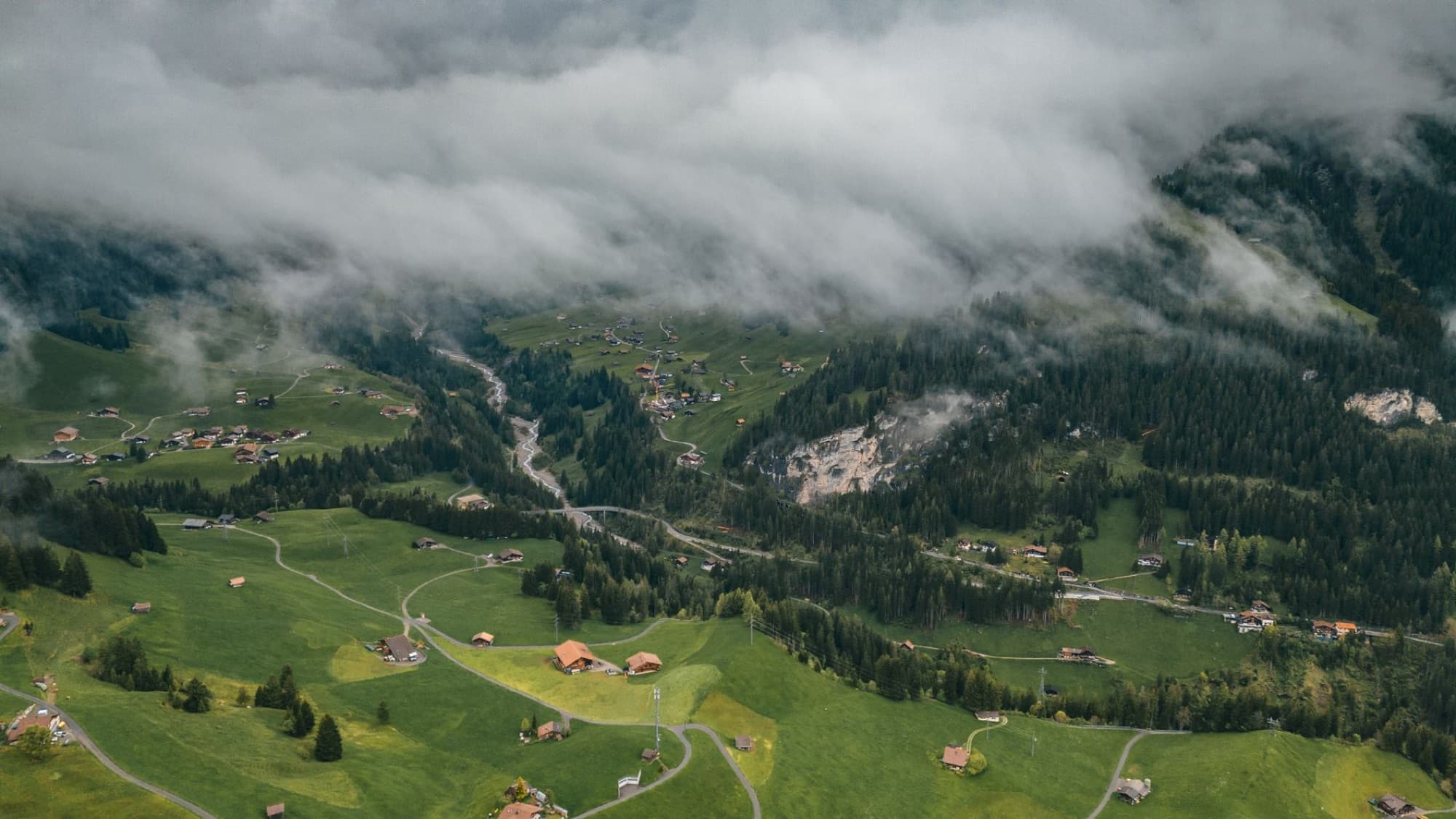 A breathtaking aerial view of a lush mountain valley dotted with cottages under a cloudy sky.