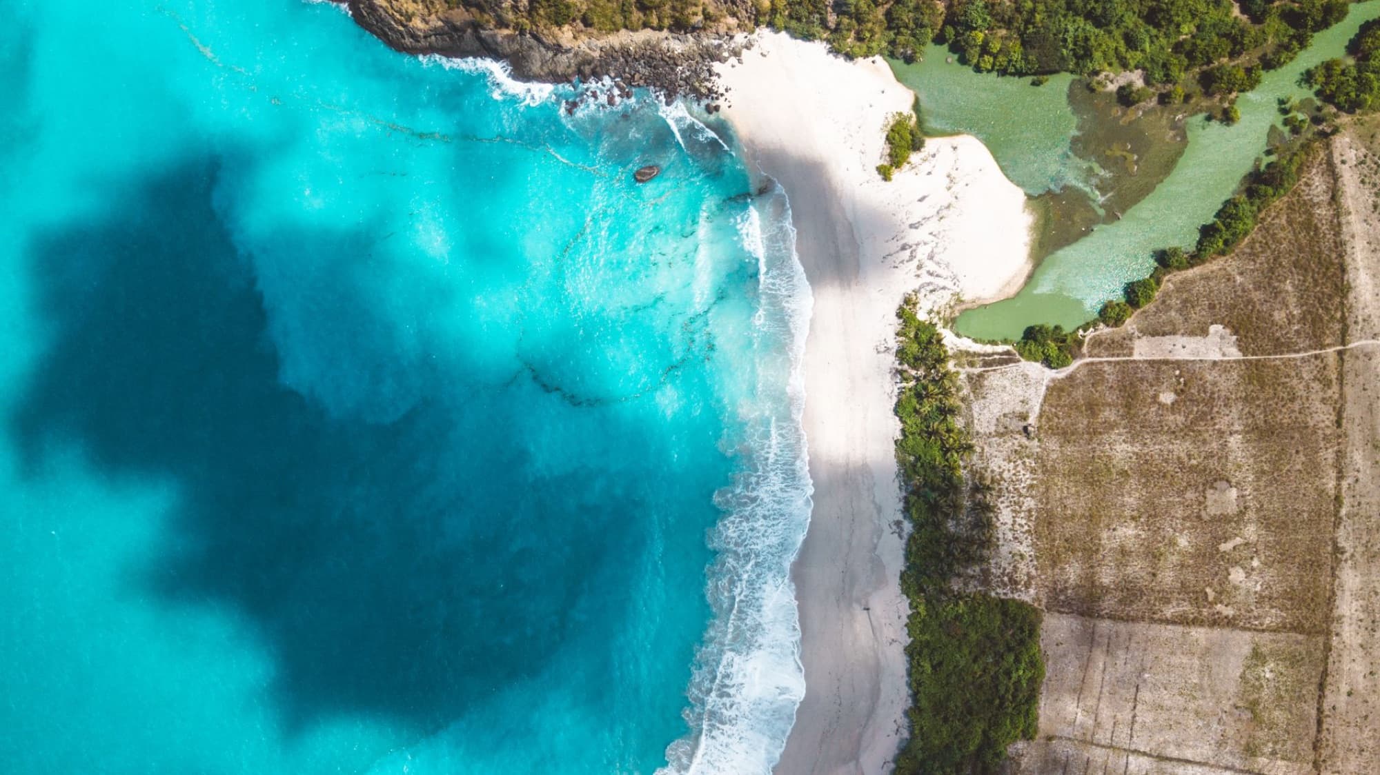 Scenic aerial view of a beautiful coastline with turquoise water, white sand, and lush greenery.