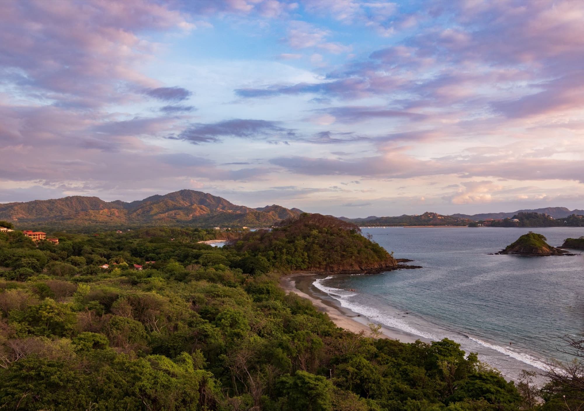 A stunning aerial view of the Guanacaste coastline at sunset with lush greenery and gentle waves.