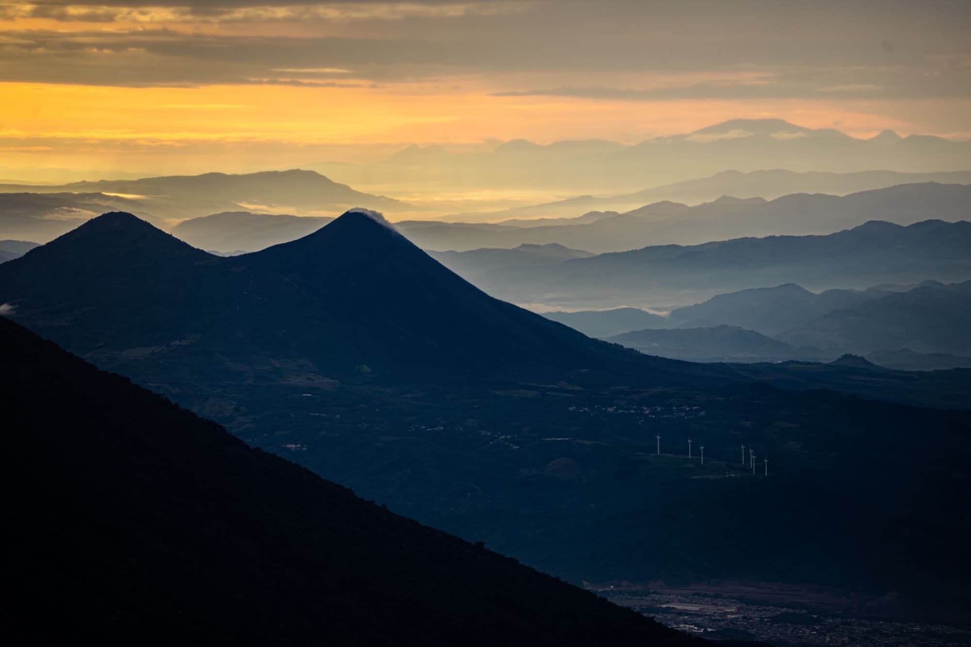 Dramatic aerial view of Guatemala's mountain ranges at sunrise with layered mist and warm hues.