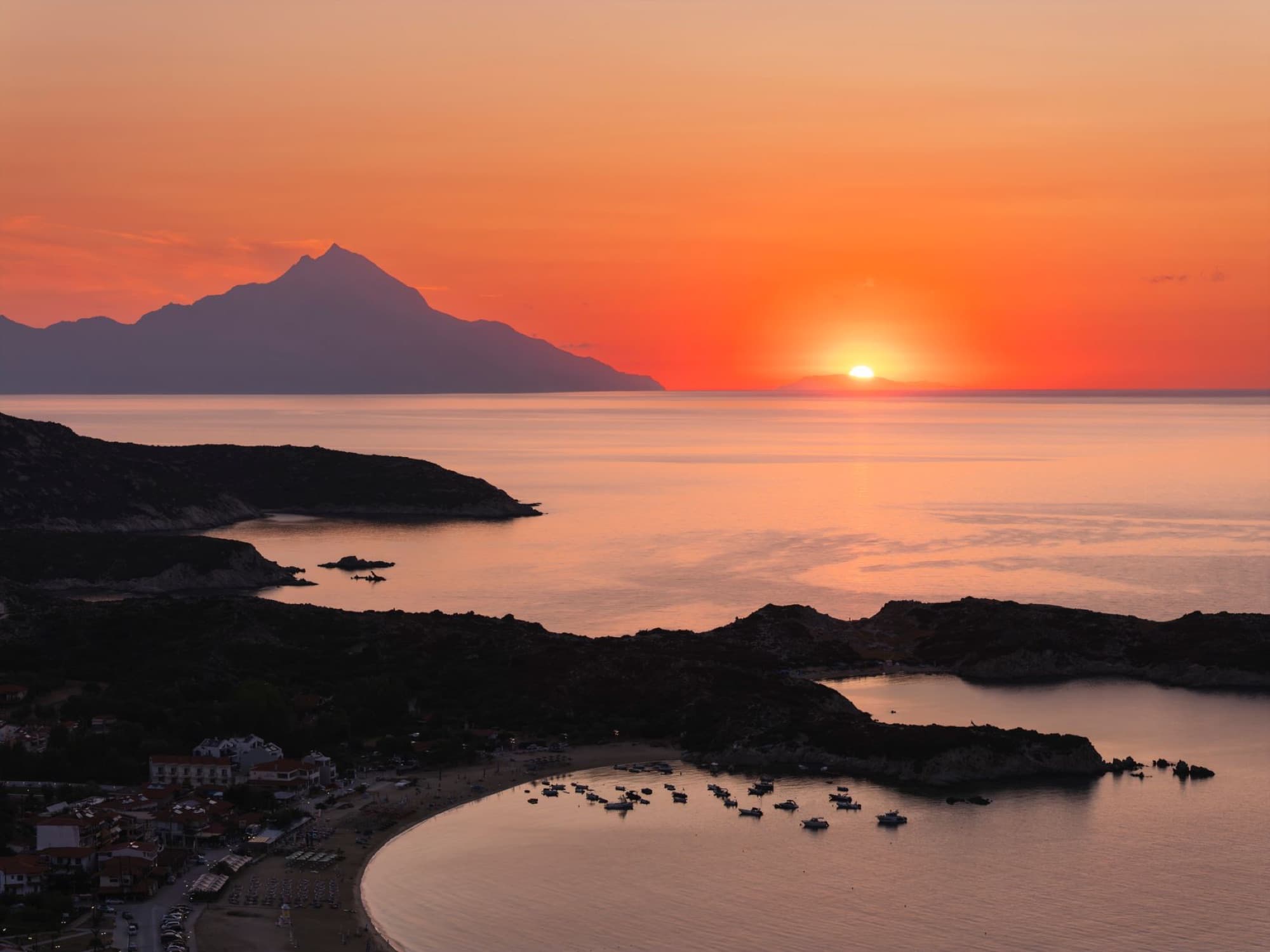 Breathtaking aerial view of sunrise over Kalamitsi Beach, Greece, surrounded by serene waters and majestic mountains.