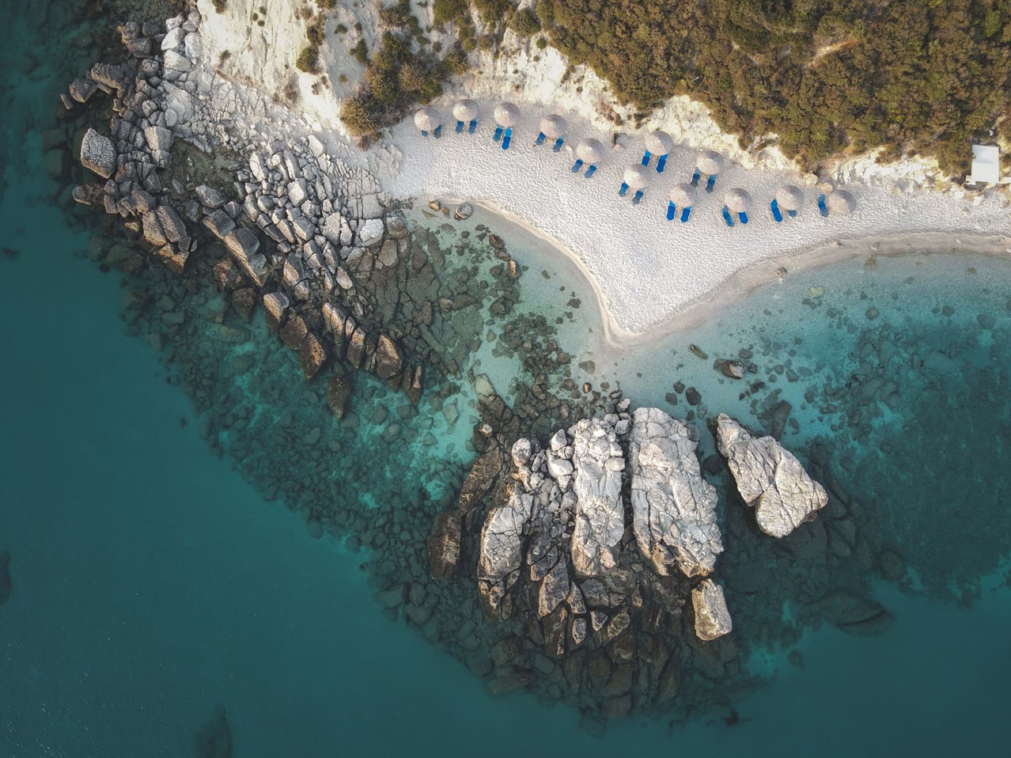 Aerial shot of a scenic Mediterranean beach with rocky cliffs and parasols, showcasing stunning turquoise waters.