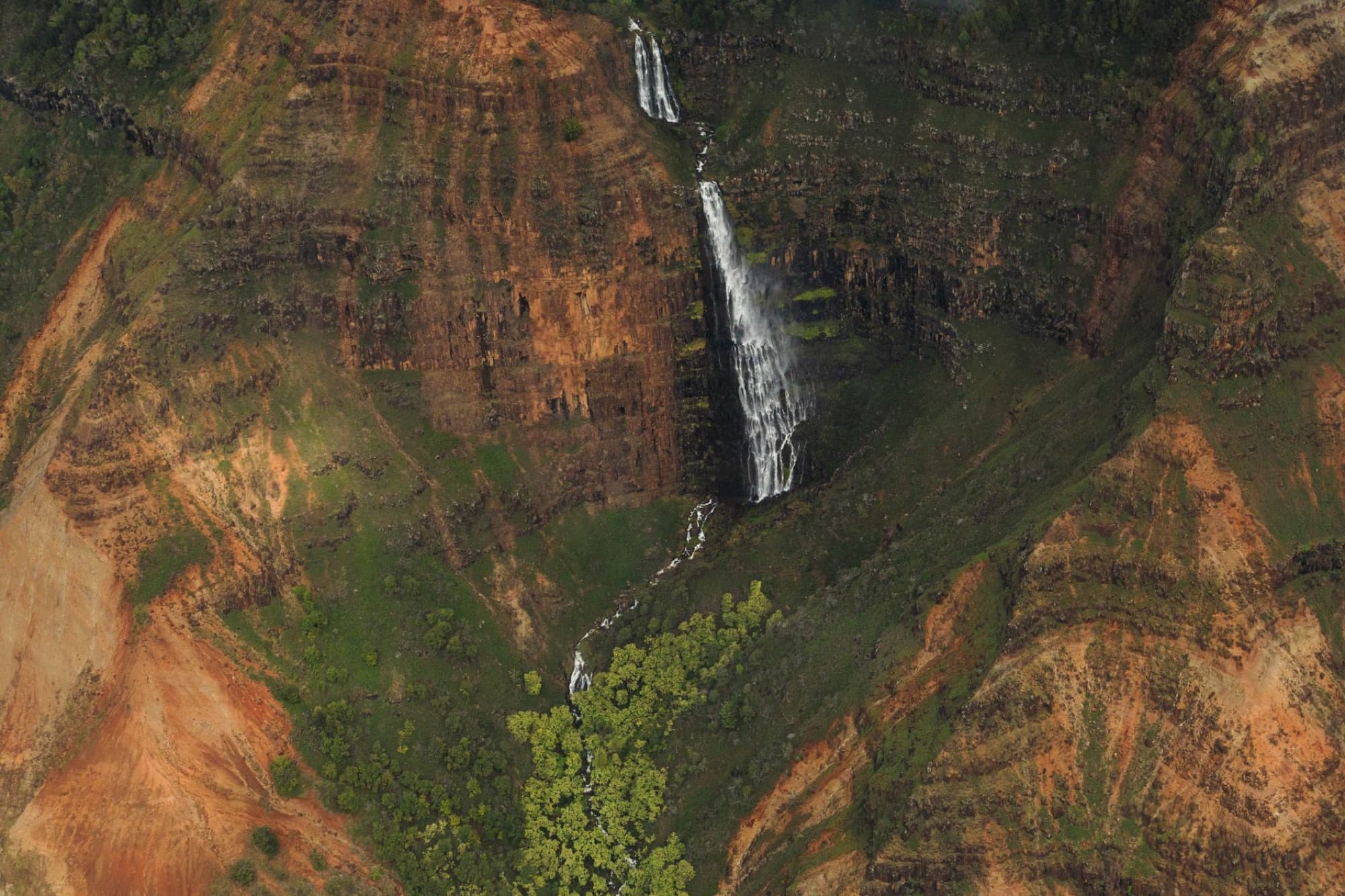 Stunning aerial shot of a waterfall cascading down Waimea Canyon's vibrant rocky cliffs in Hawaii.