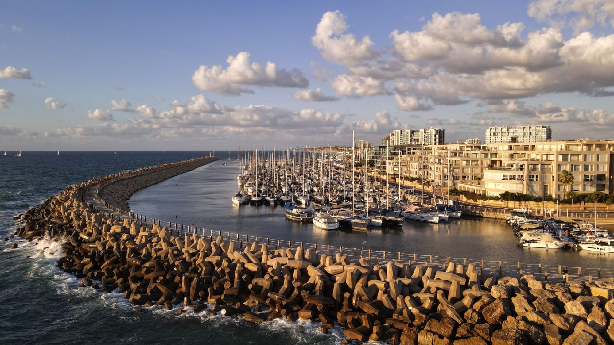 A stunning aerial shot of Herzliya Marina, Israel, showcasing boats and a breakwater at sunset.