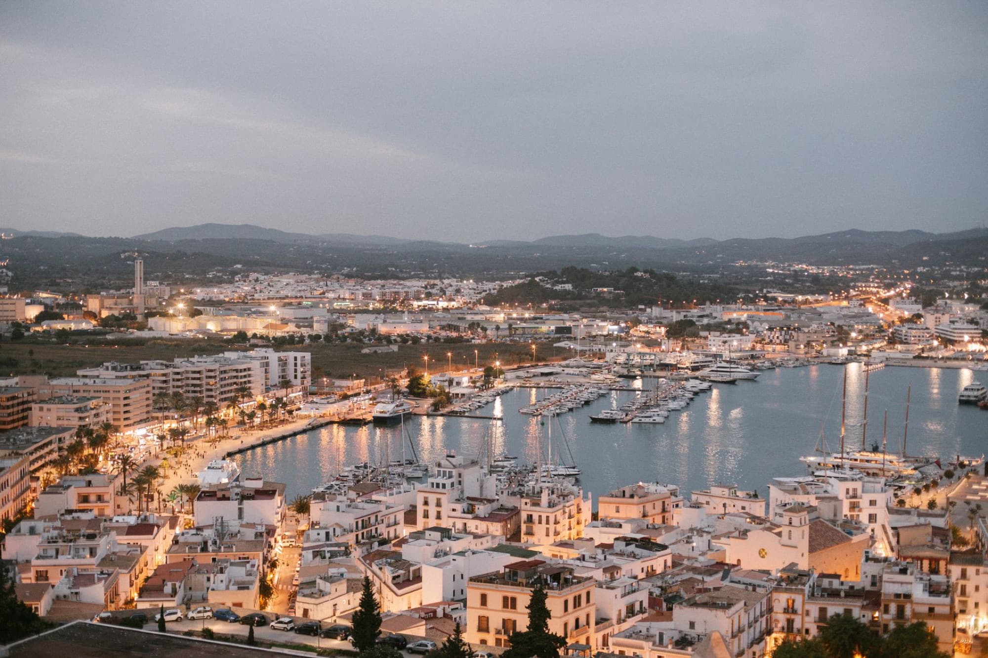 A scenic aerial view of Ibiza's marina at dusk, showcasing vibrant city lights and bustling harbor in Spain.