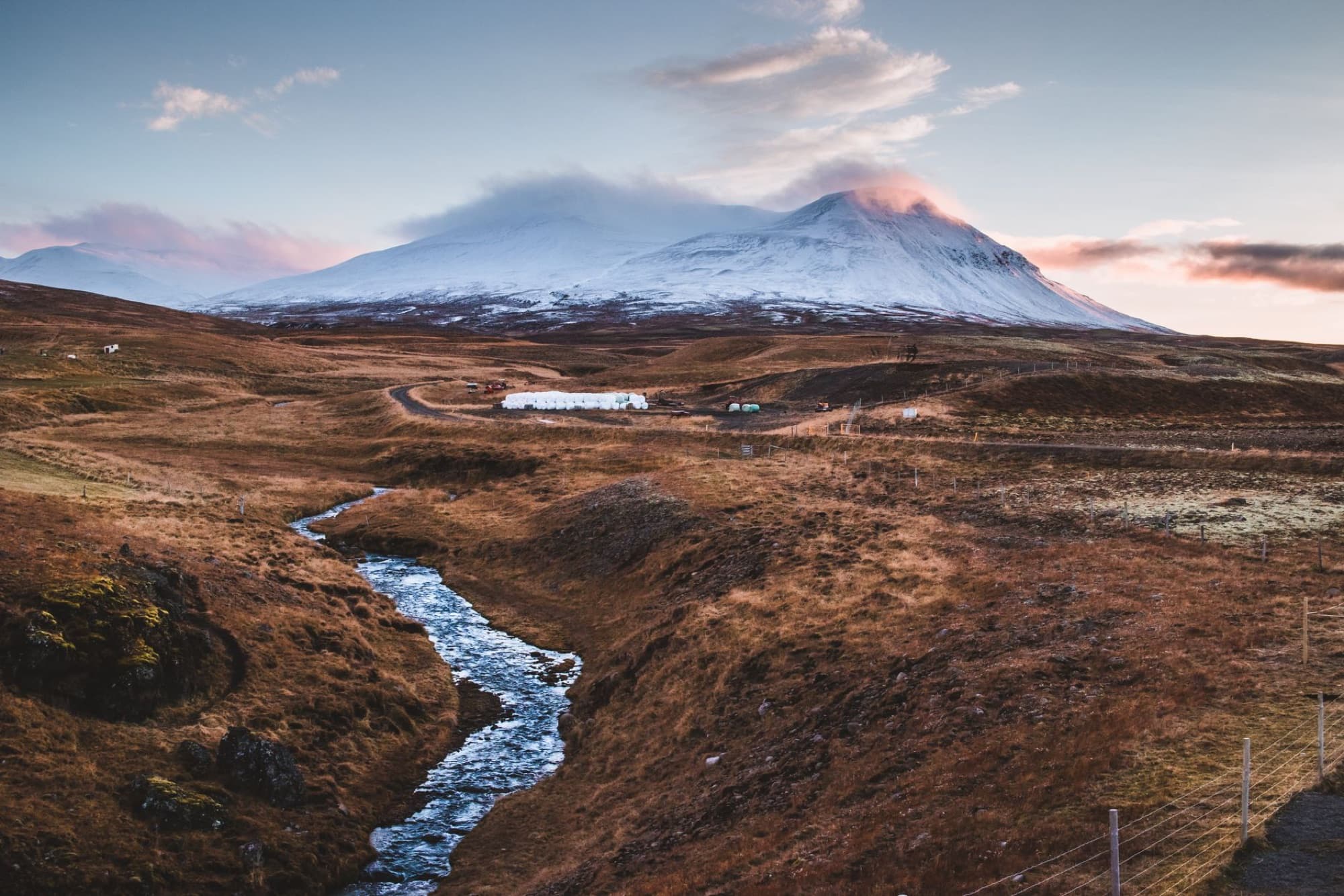 Scenic view of an Icelandic mountain with stream at sunrise, featuring snow-capped peaks and autumn landscape.