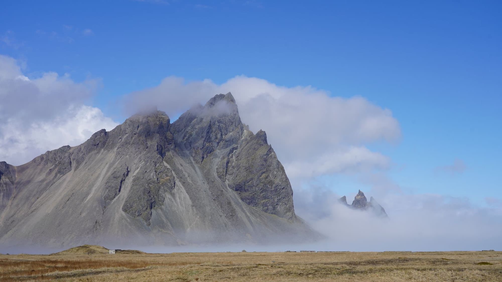Scenic view of Icelandic mountains with clouds and blue sky, offering a tranquil landscape.
