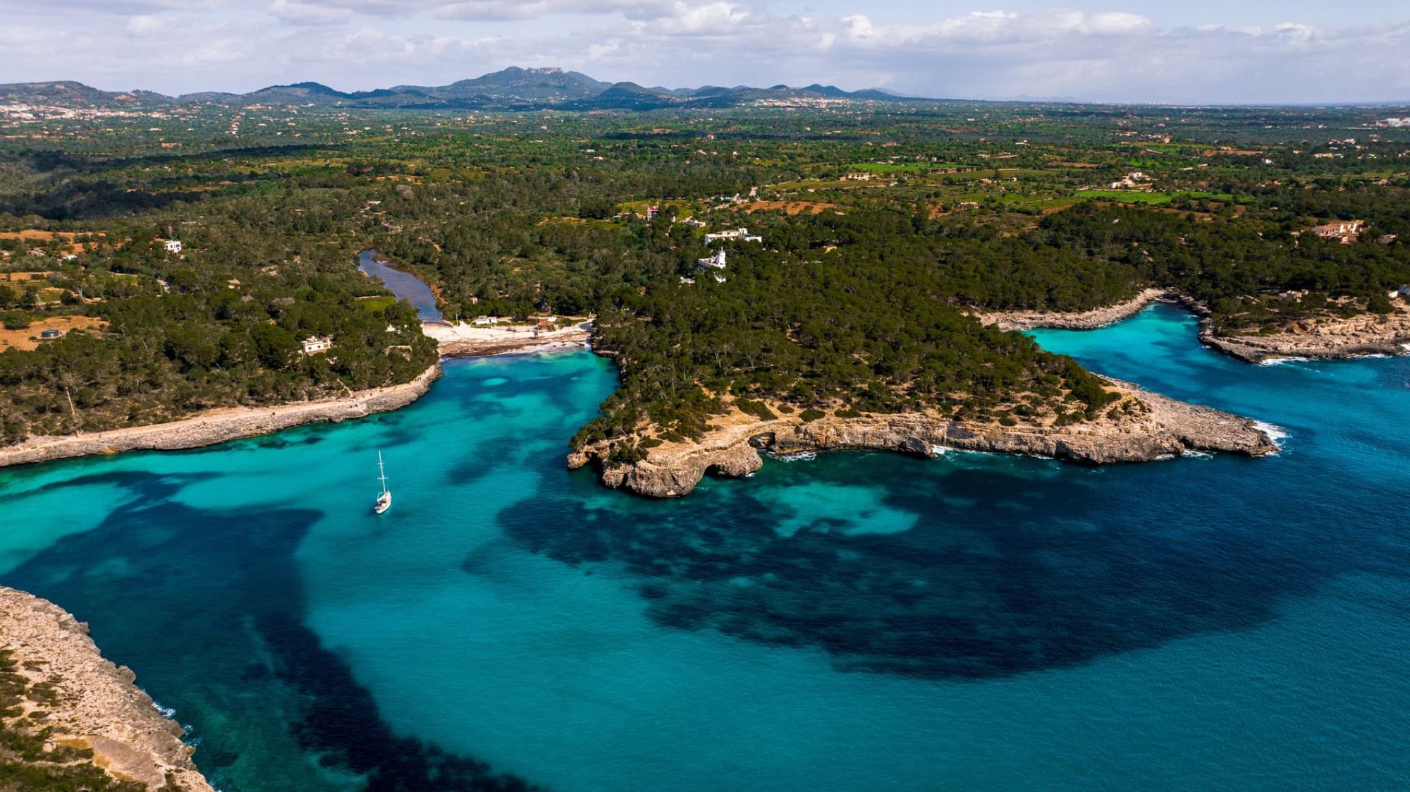 Aerial view of Mallorca's coastline with turquoise waters, cliffs, and lush greenery under a clear sky.