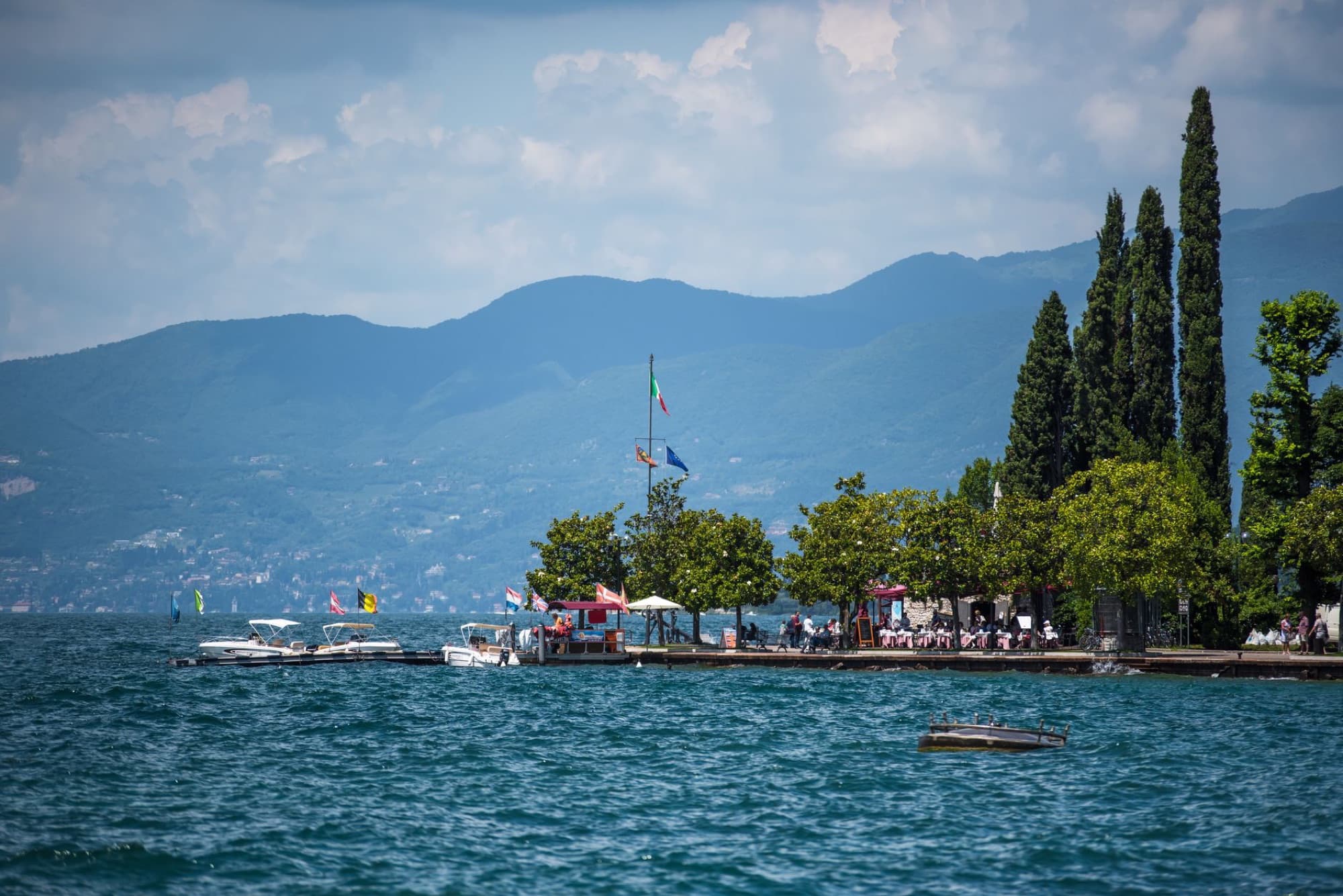 A picturesque Italian lakeside scene with boats and mountains, perfect for a summer getaway.
