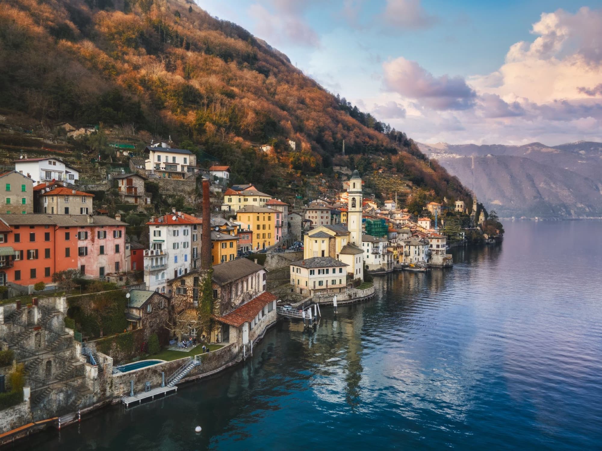A picturesque aerial view of a charming town along Lake Como, surrounded by mountains and water.