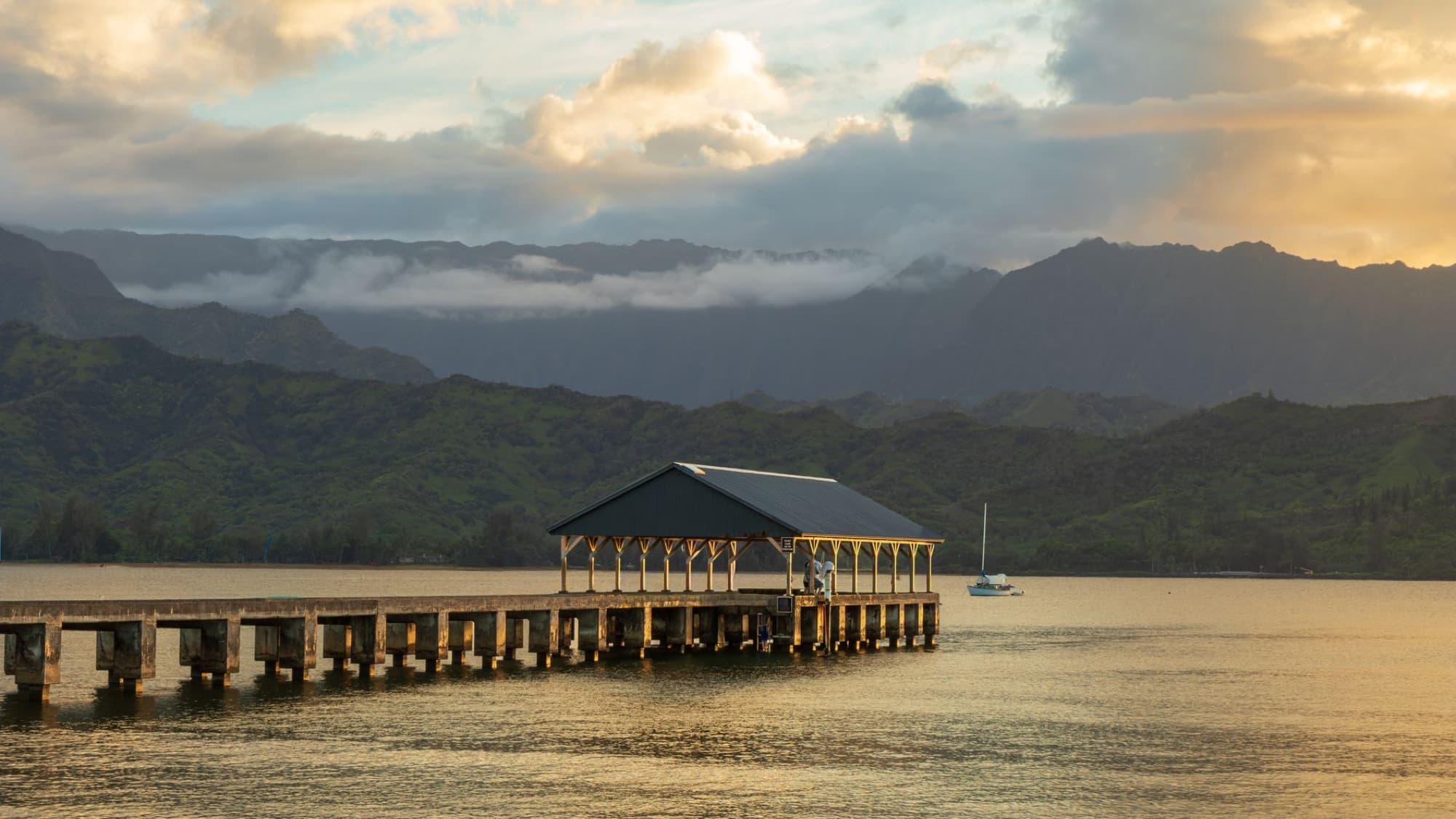 Picturesque view of Hanalei Pier with mountains and sunset in Kauai, Hawaii.