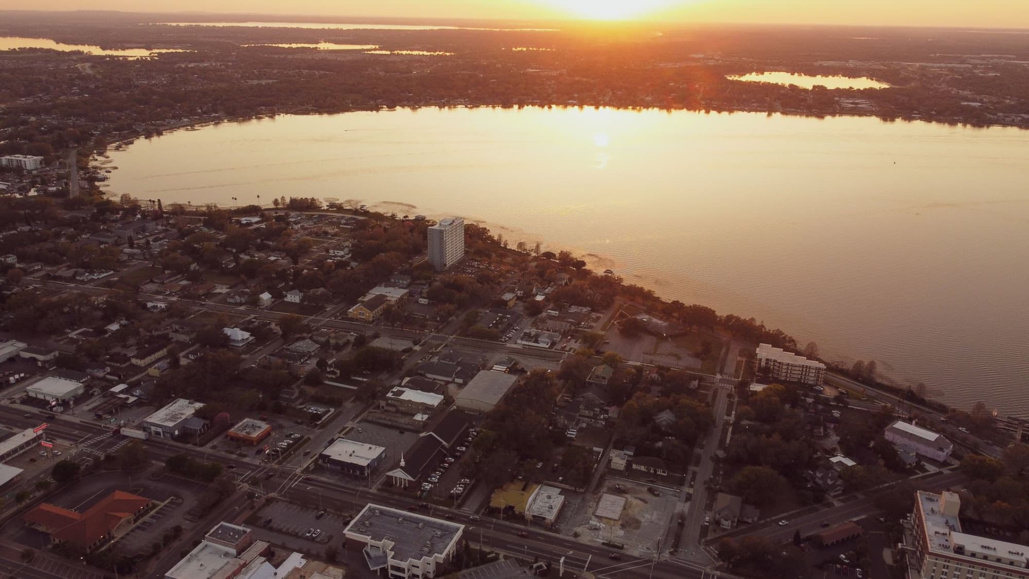 A beautiful aerial view capturing a cityscape at sunset beside a shimmering lake, creating a serene and warm atmosphere.