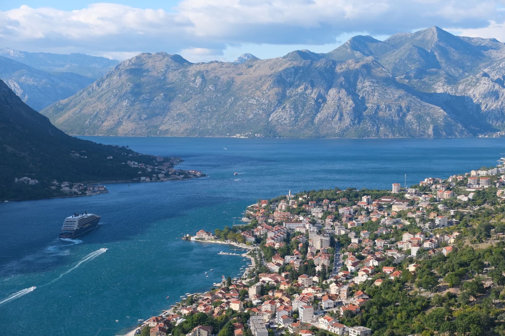 Stunning aerial photo of Kotor Bay with mountains and a cruise ship on a sunny day.