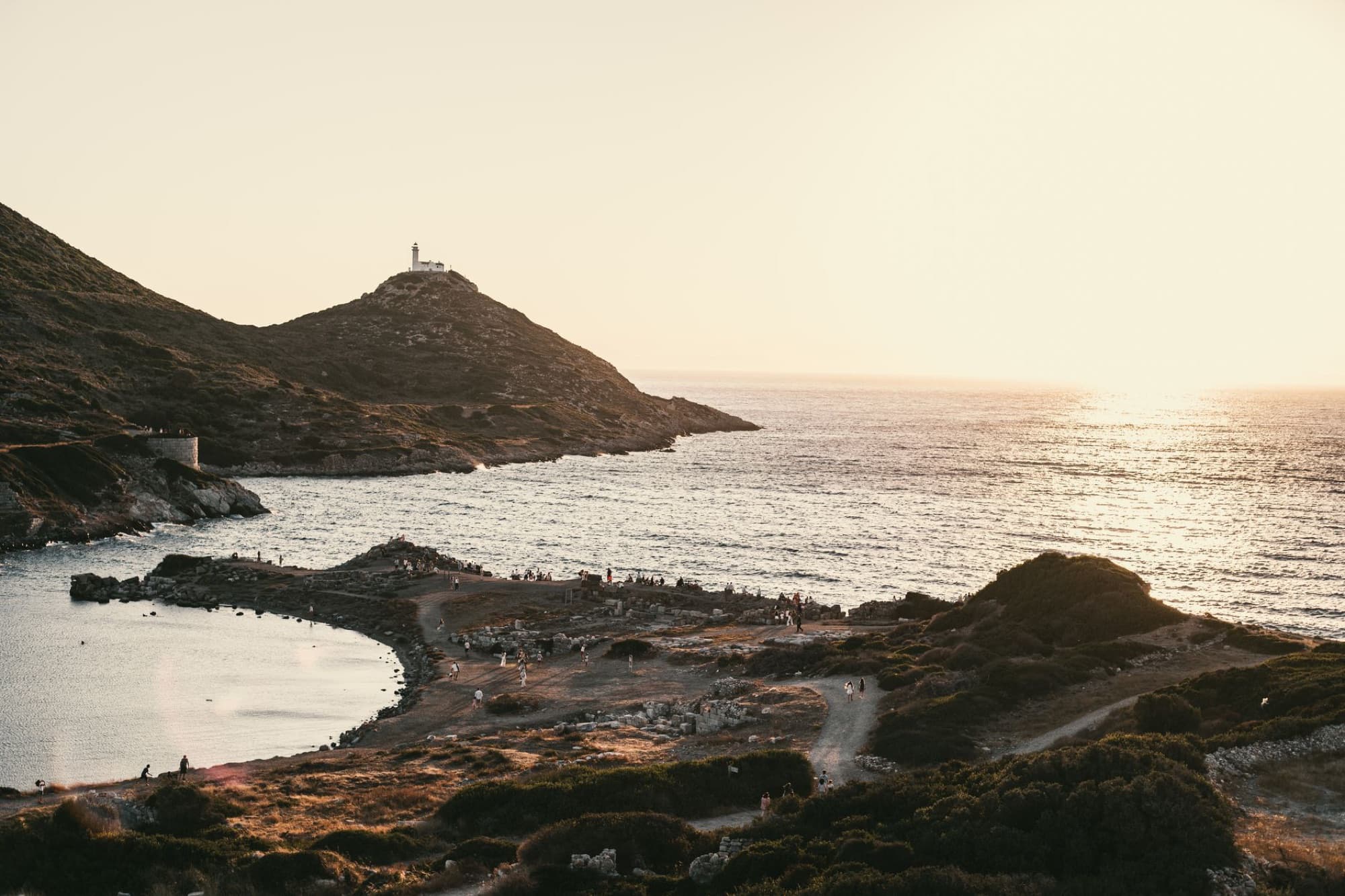 Scenic coastal landscape featuring a lighthouse at sunset with a calm sea.
