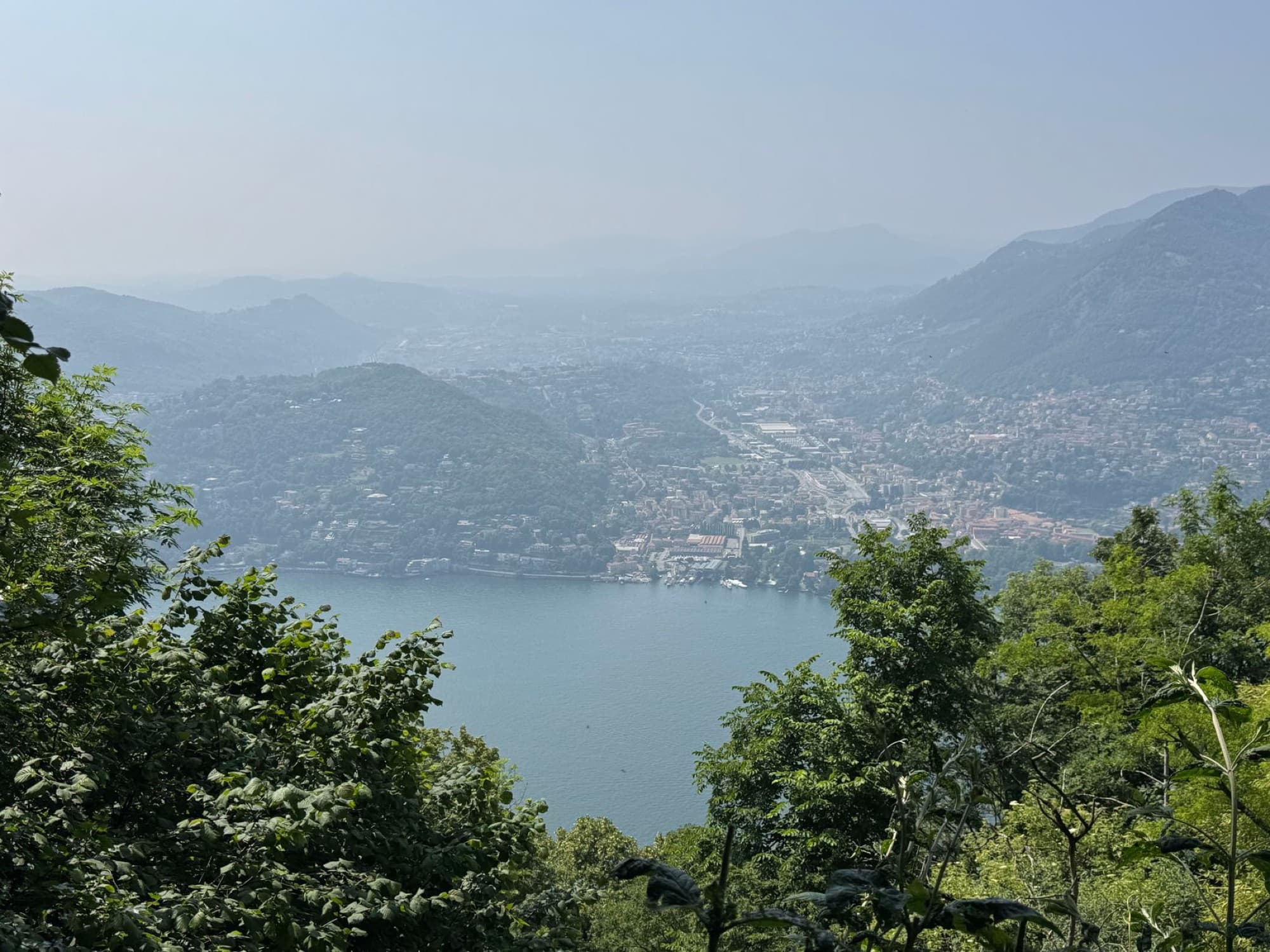 A picturesque aerial view of Lake Como surrounded by lush greenery and distant mountains.