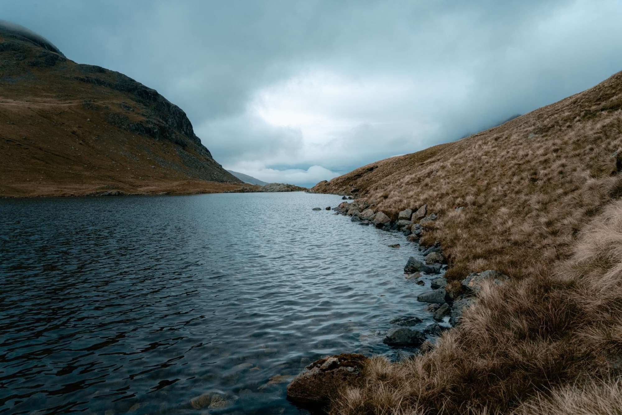 Tranquil mountain lake in England's Lake District with overcast sky and rugged terrain.