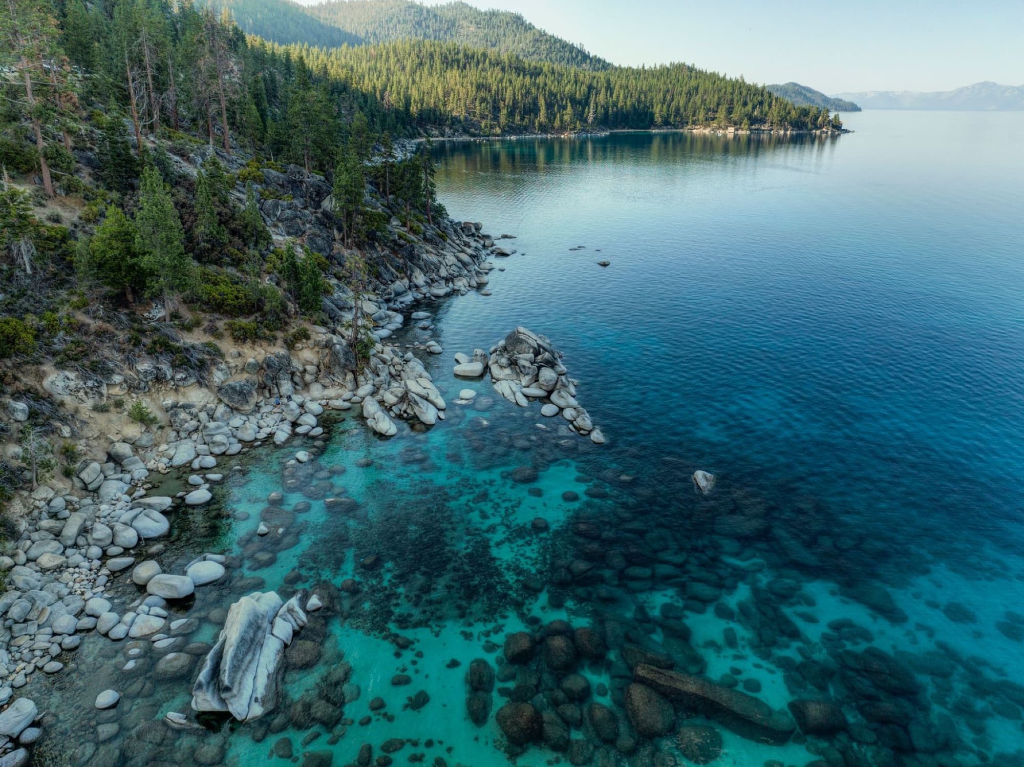 Aerial view of Lake Tahoe's tranquil coastline, showcasing crystal-clear waters and forested landscape.