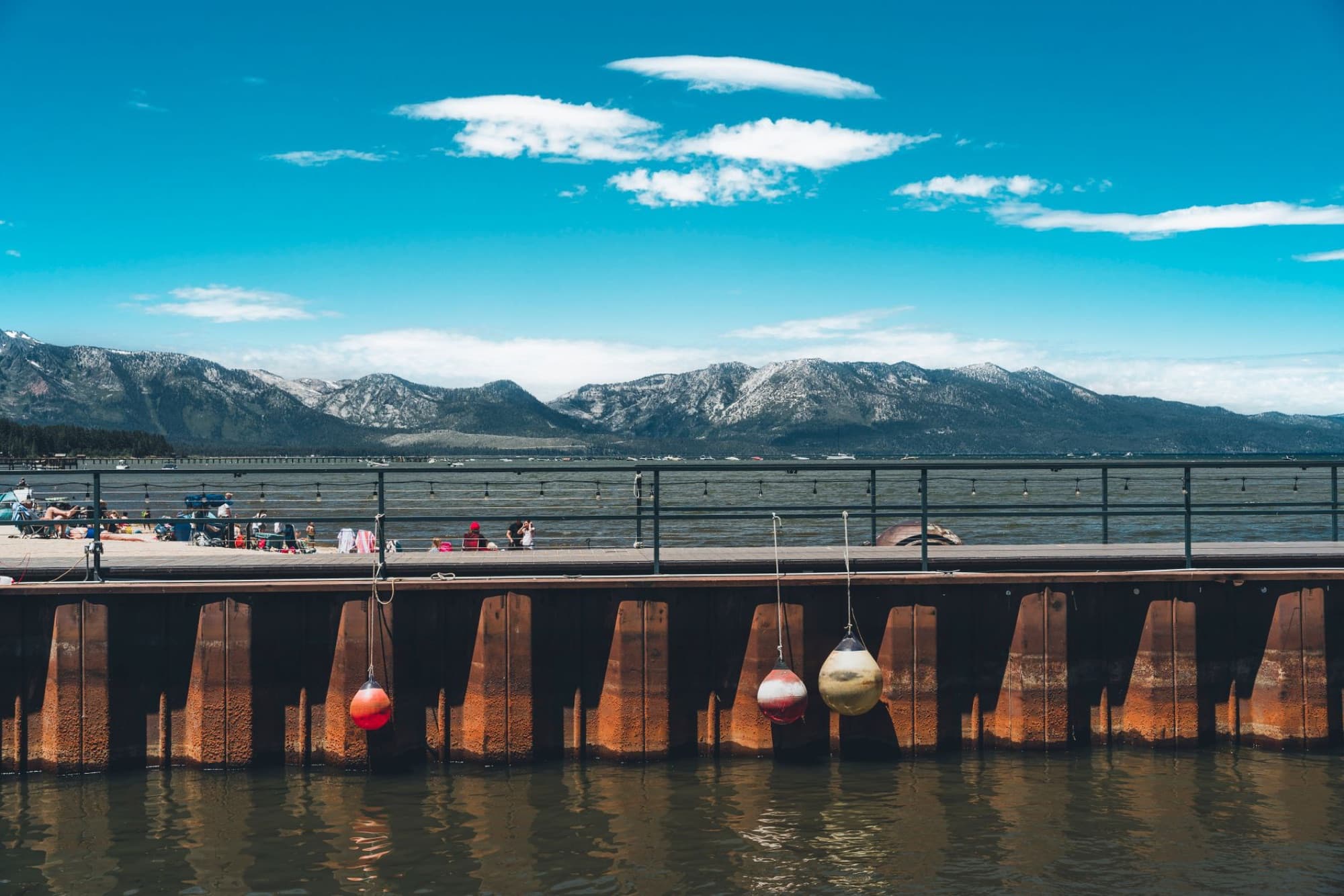 Enjoy a sunny day at Lake Tahoe with mountains and a bustling boardwalk.