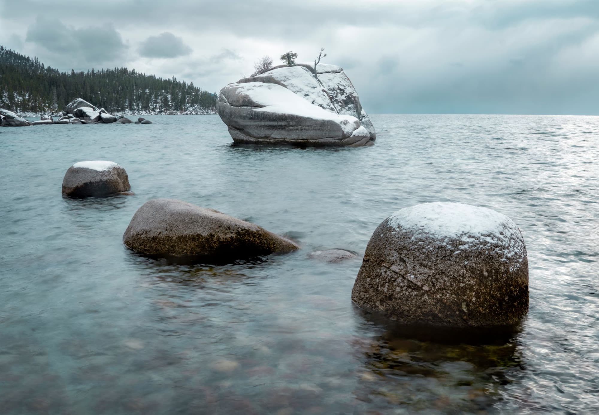 Serene winter scene of snow-covered rocks by Lake Tahoe in a tranquil, scenic setting.