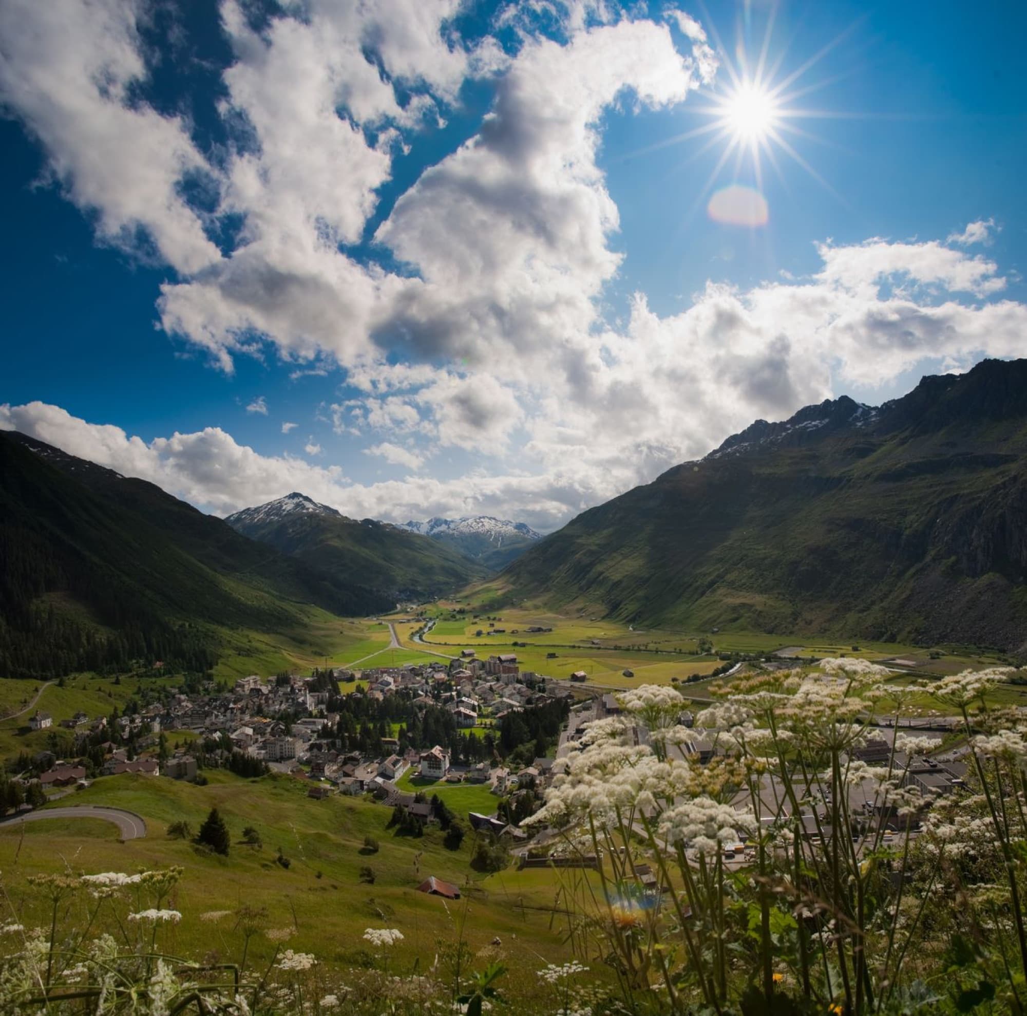 Picturesque mountain village under a bright sun with lush valley and rugged peaks.