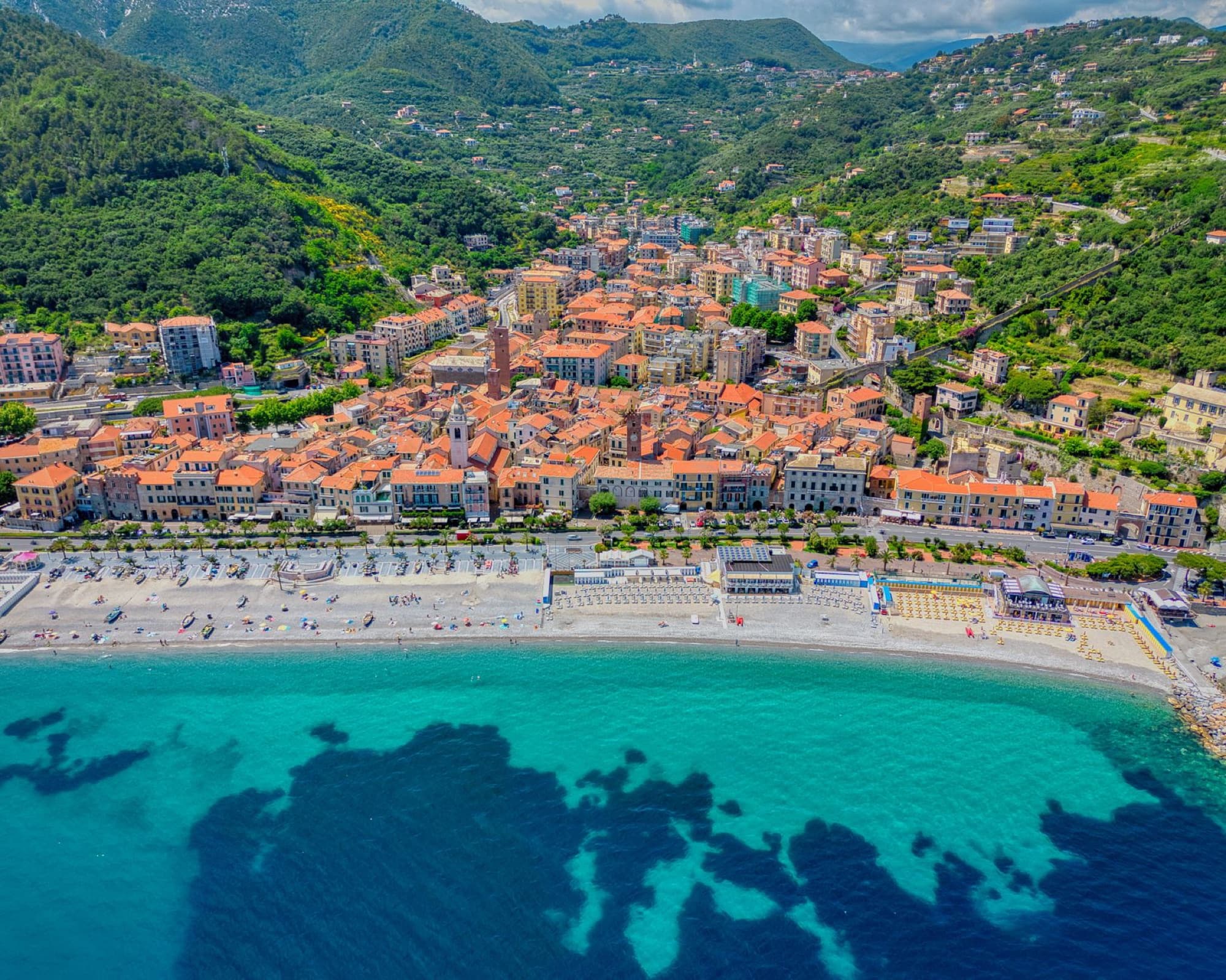 Aerial view showing the picturesque coastal town of Noli, Liguria, with its vibrant rooftops and azure sea.