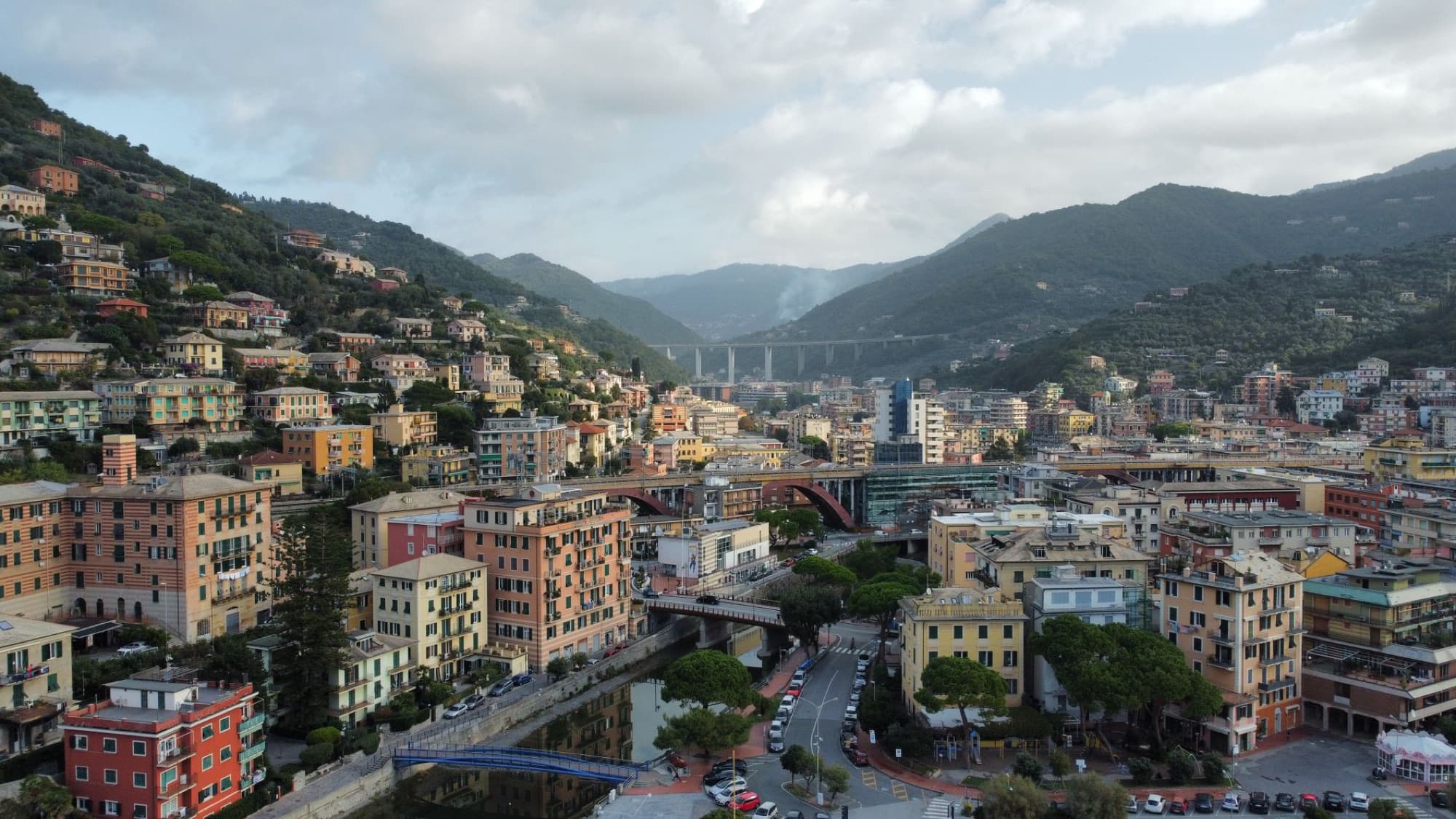 Aerial view of Recco, Liguria showcasing colorful buildings and scenic mountains under cloudy skies.