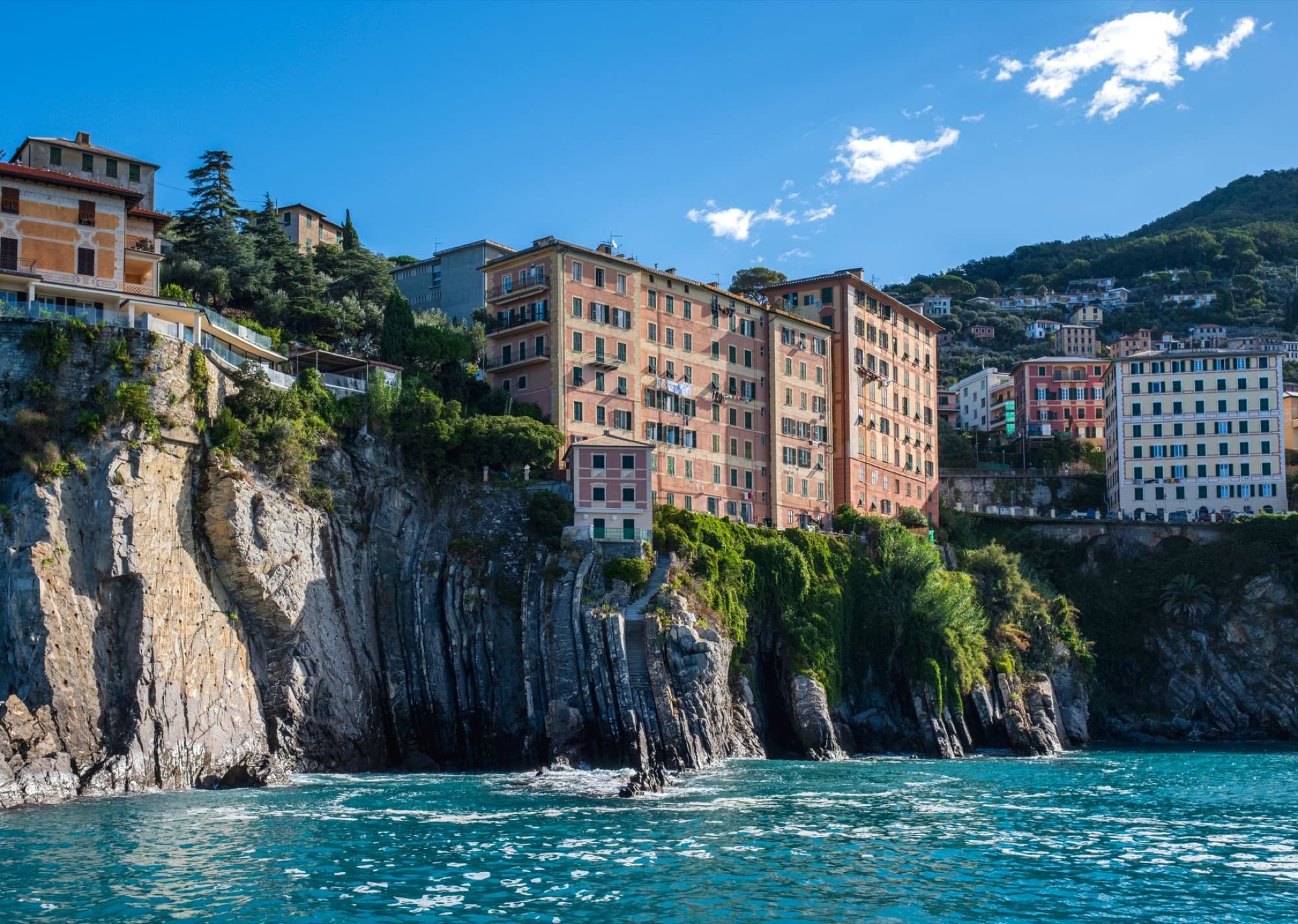 Charming old buildings atop rocky cliffs along Italy's Ligurian coastline on a sunny day.