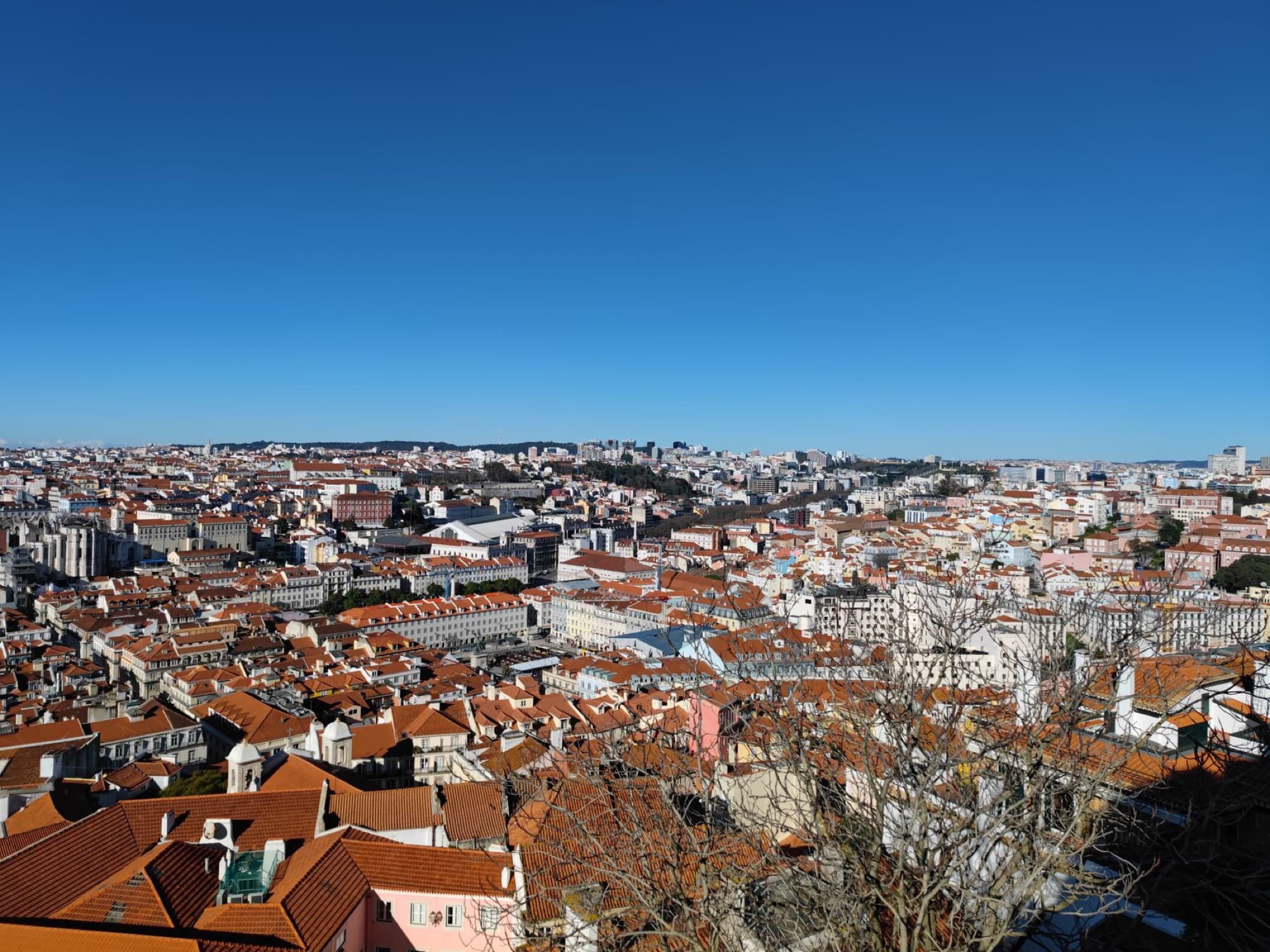 A stunning aerial cityscape of Lisbon, showcasing its red rooftops under a clear blue sky.